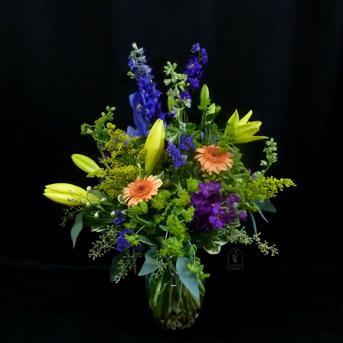 Mixed bouquet of lilies, gerbera daisies, and purple flowers in a glass vase