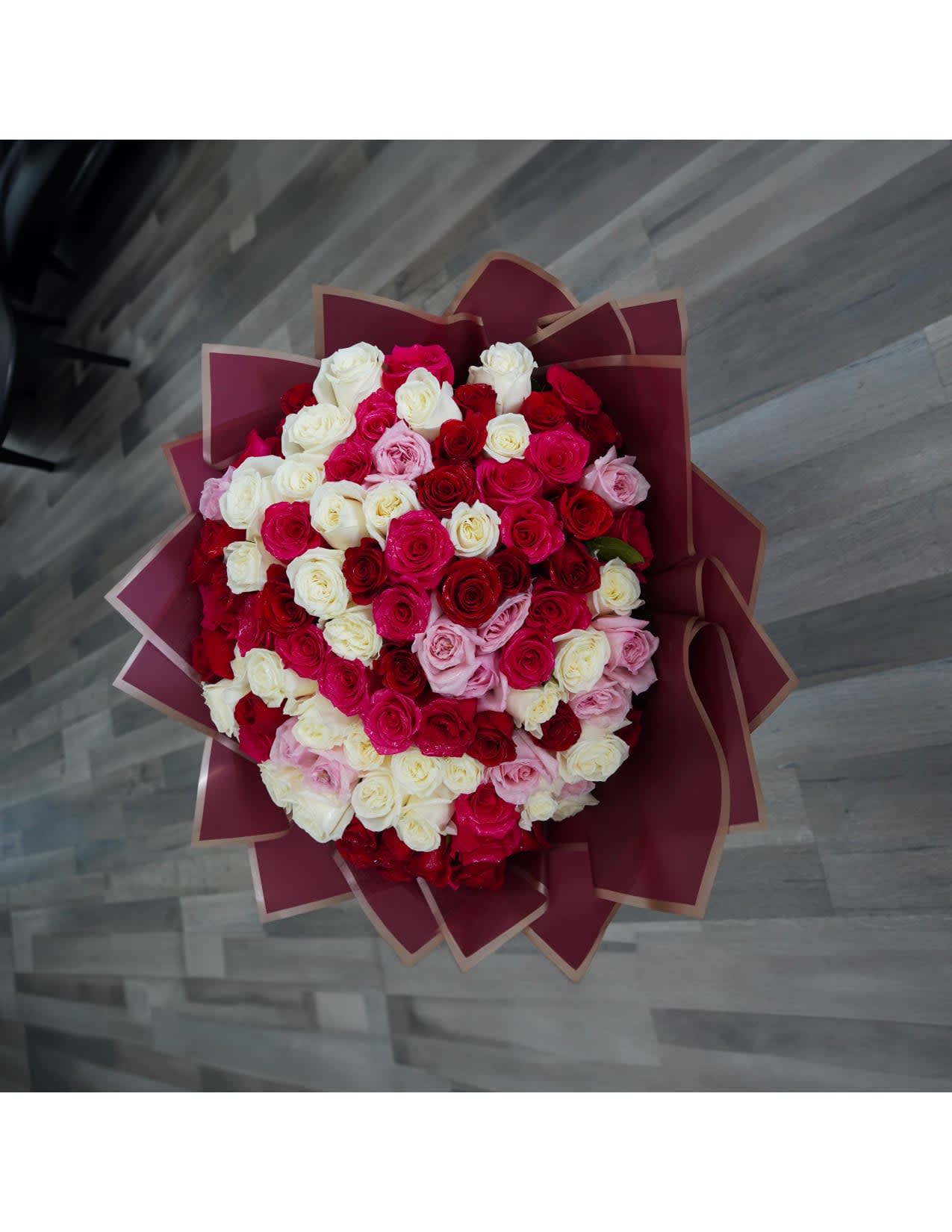 Large bouquet of red, pink, and white roses wrapped in burgundy paper