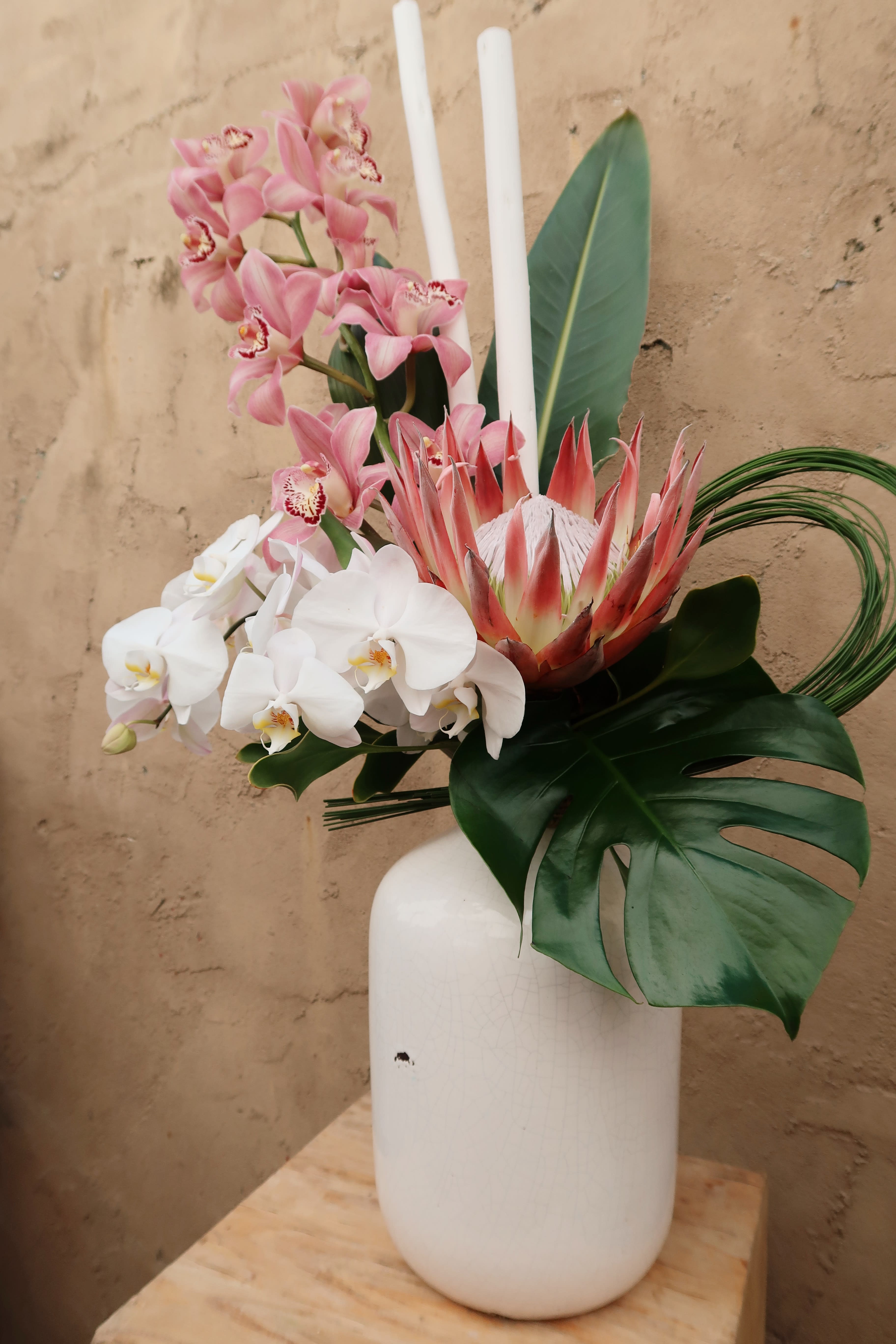 Pink and white orchids with a protea in a white vase