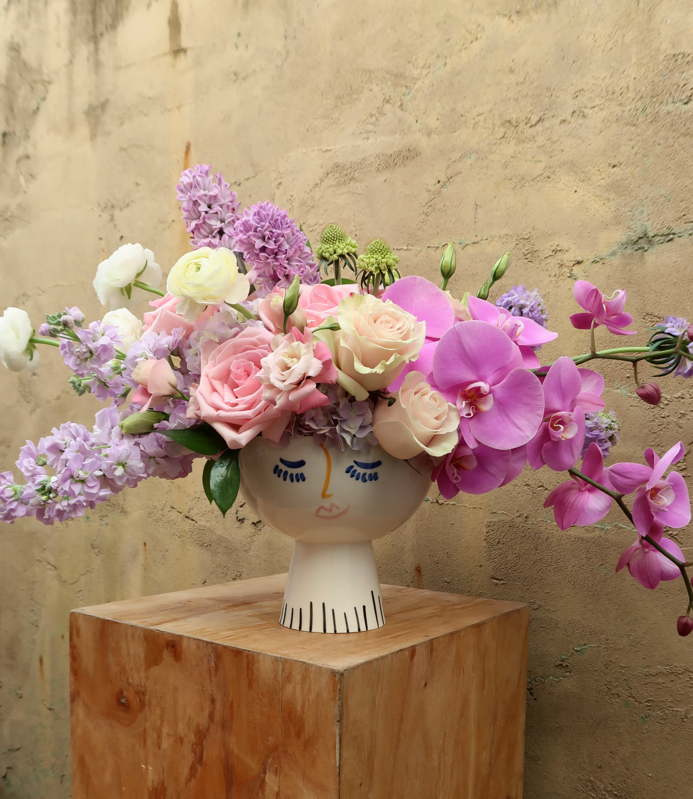Pink and lavender flowers arranged in a face-shaped vase