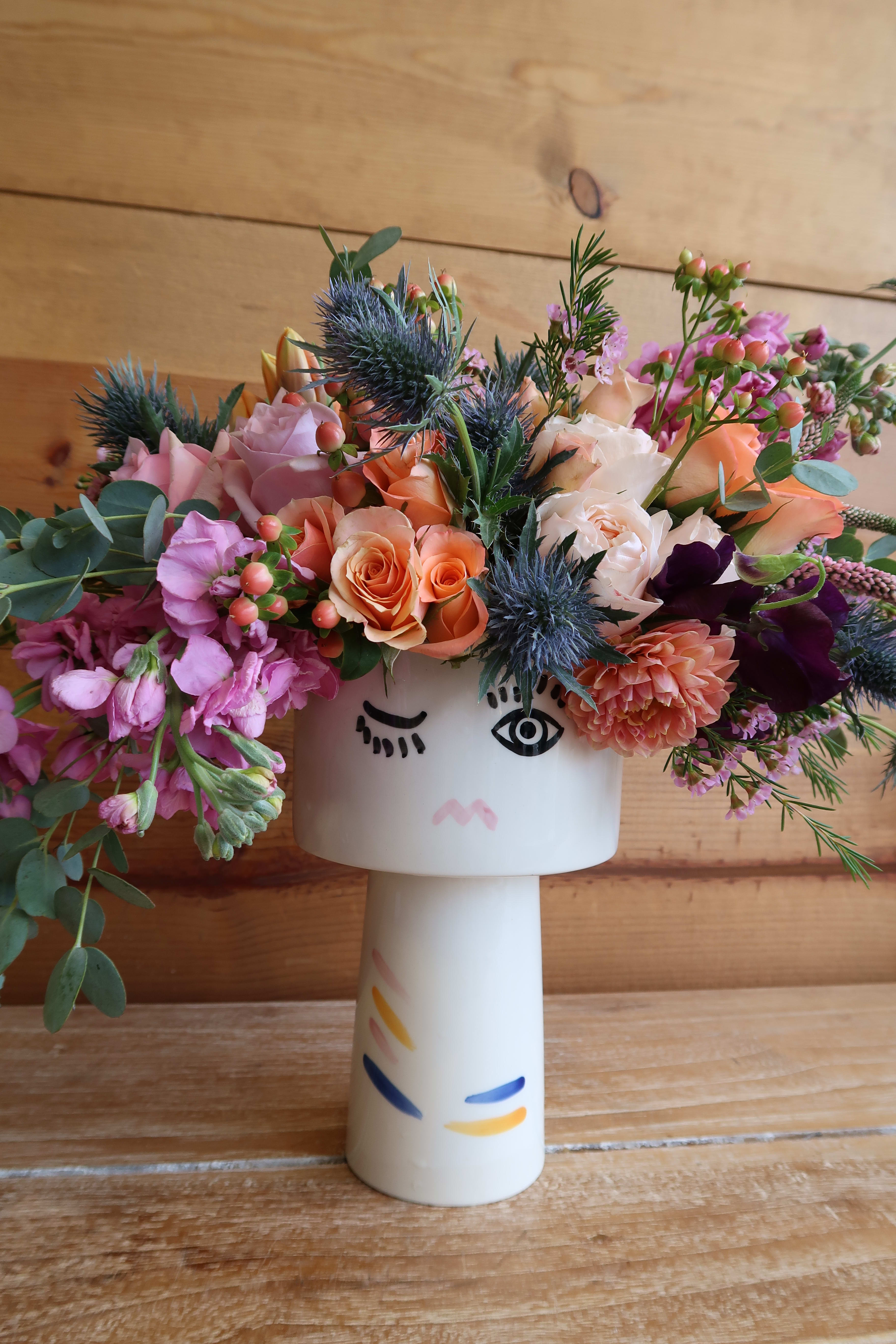 Mixed bouquet in a white face vase with pink, peach, and purple flowers