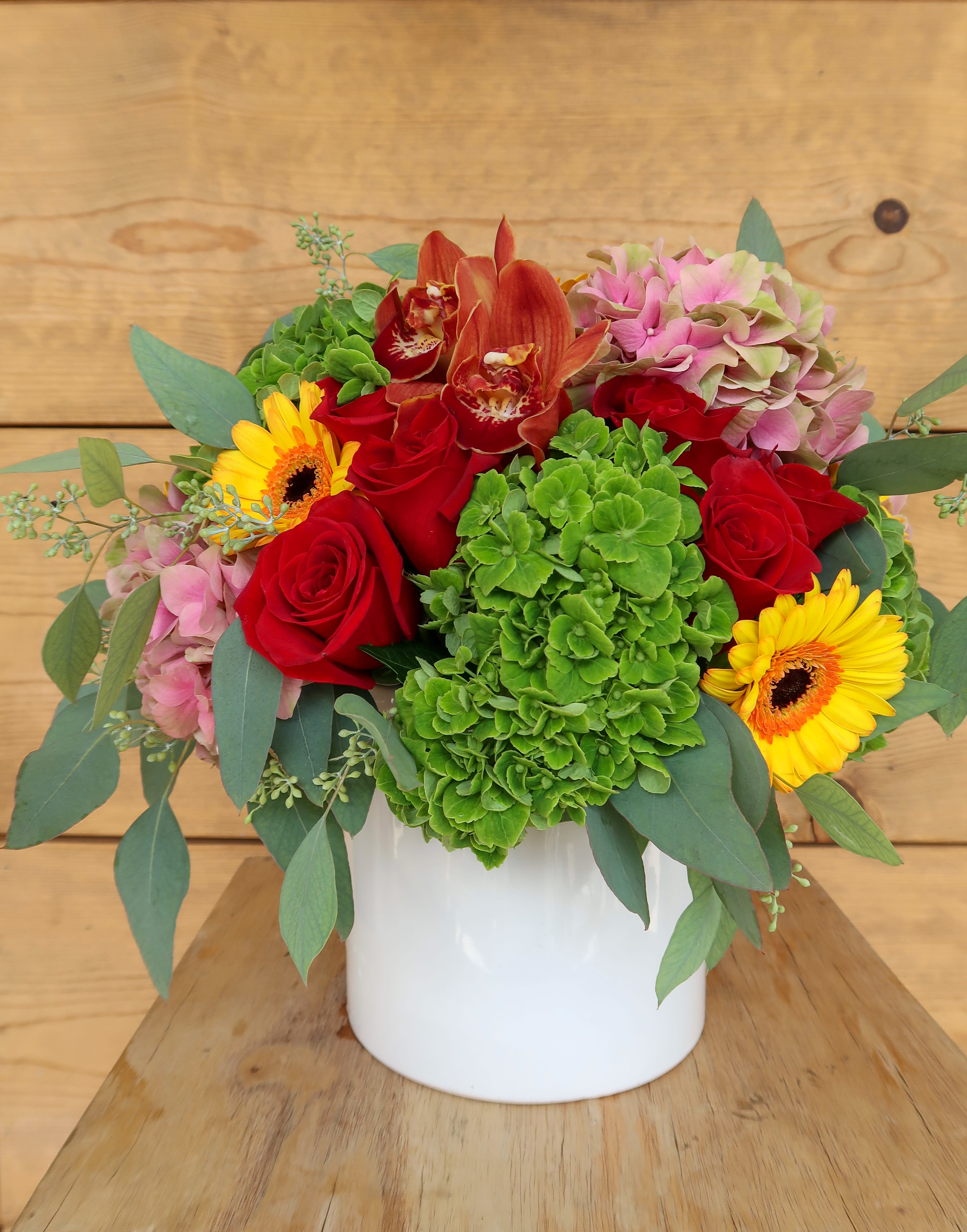 Bouquet of red roses, green hydrangea, and yellow gerbera daisies in a white vase