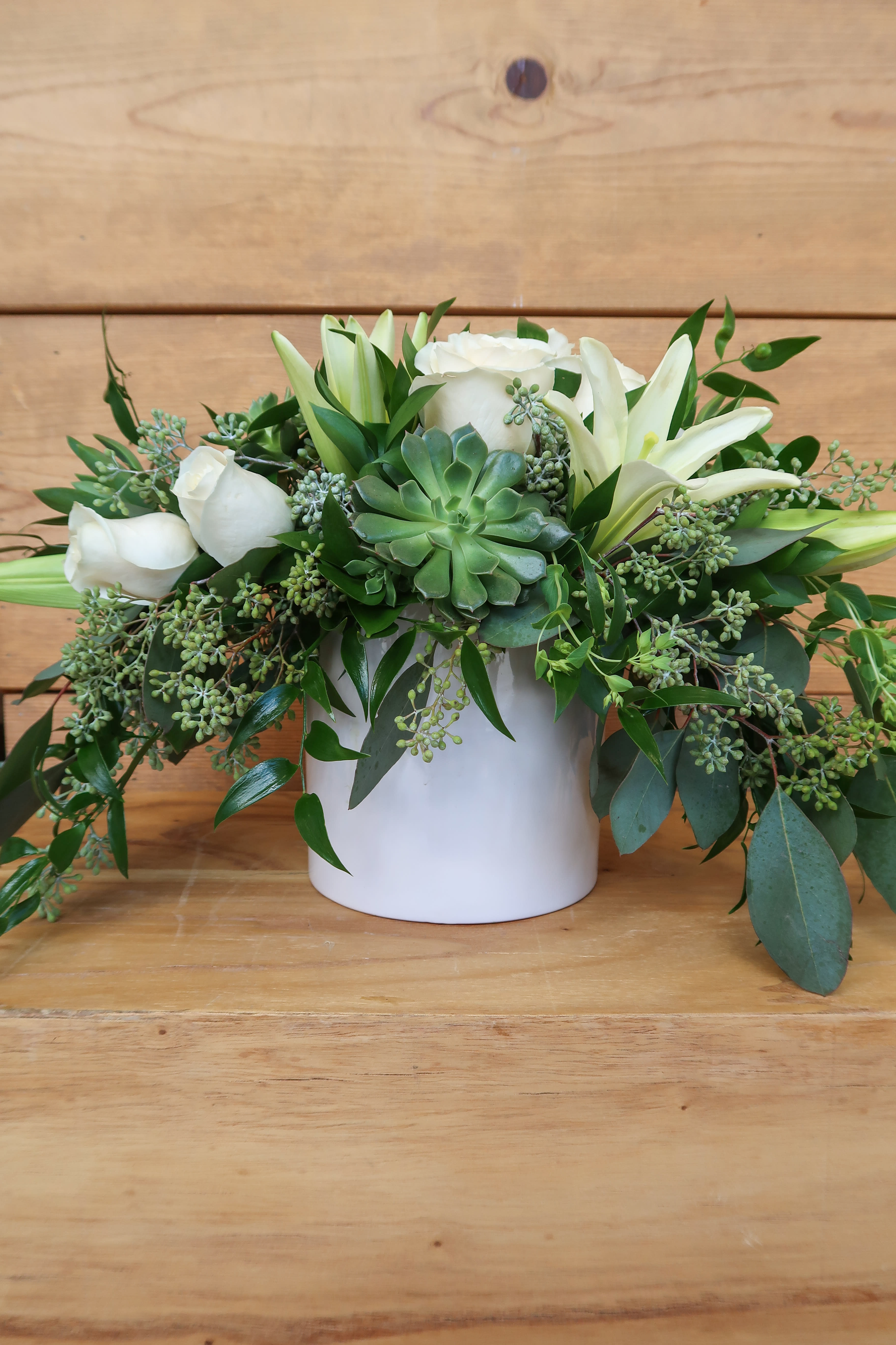 White roses and lilies arranged with a succulent in a white vase