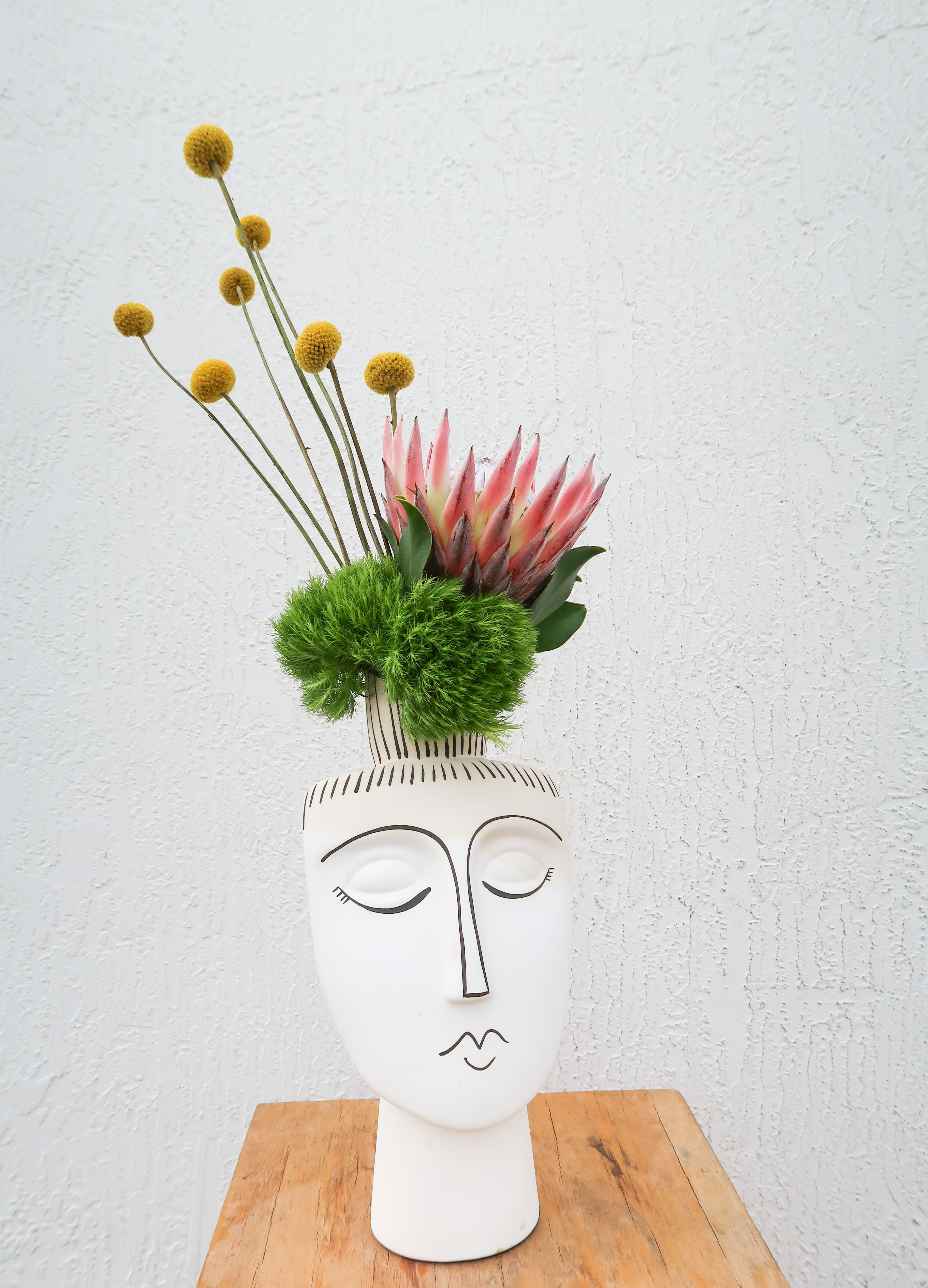 Modern floral arrangement in a white face vase with pink protea and yellow globe flowers