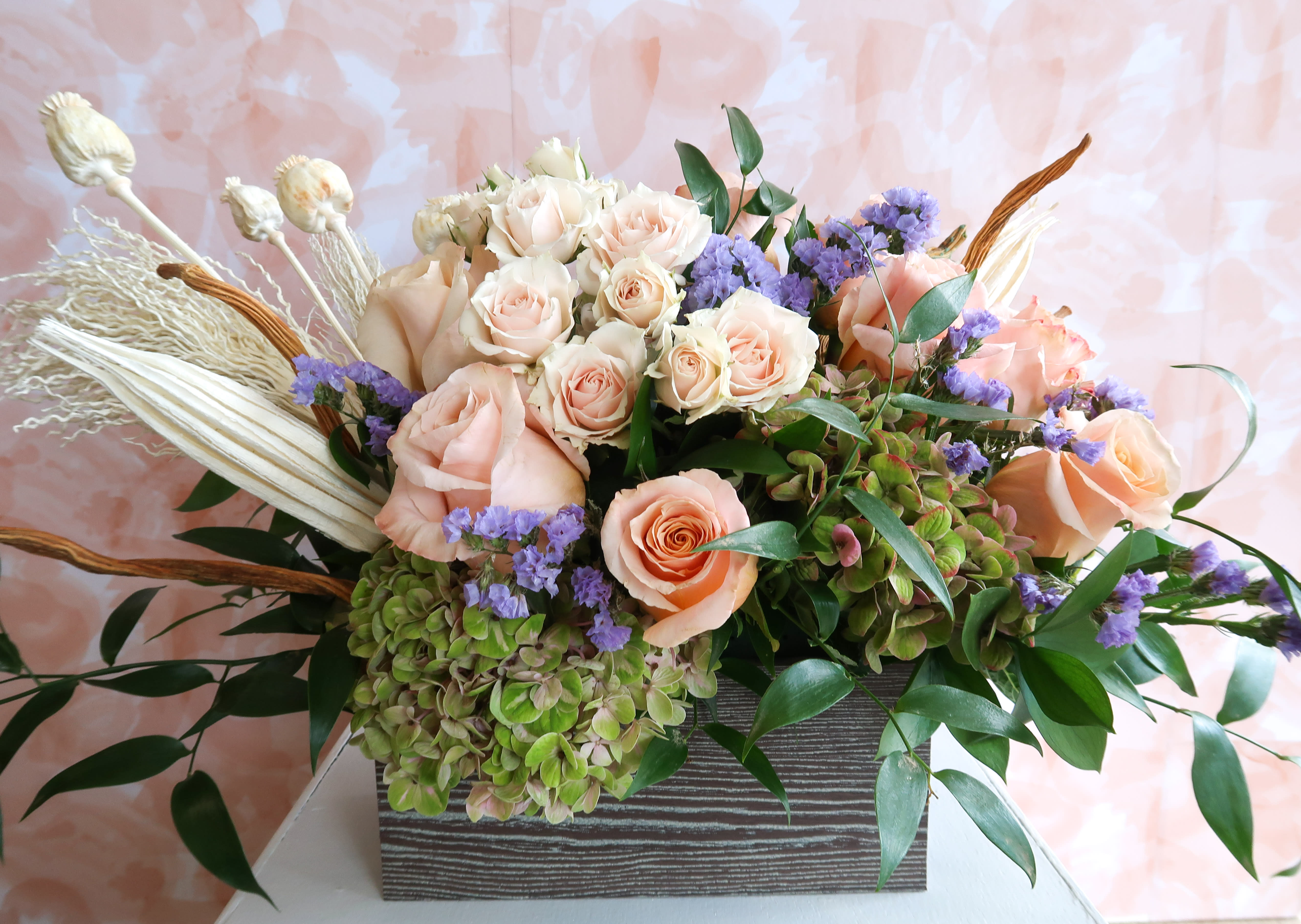 Peach roses and purple filler flowers in a rectangular vase