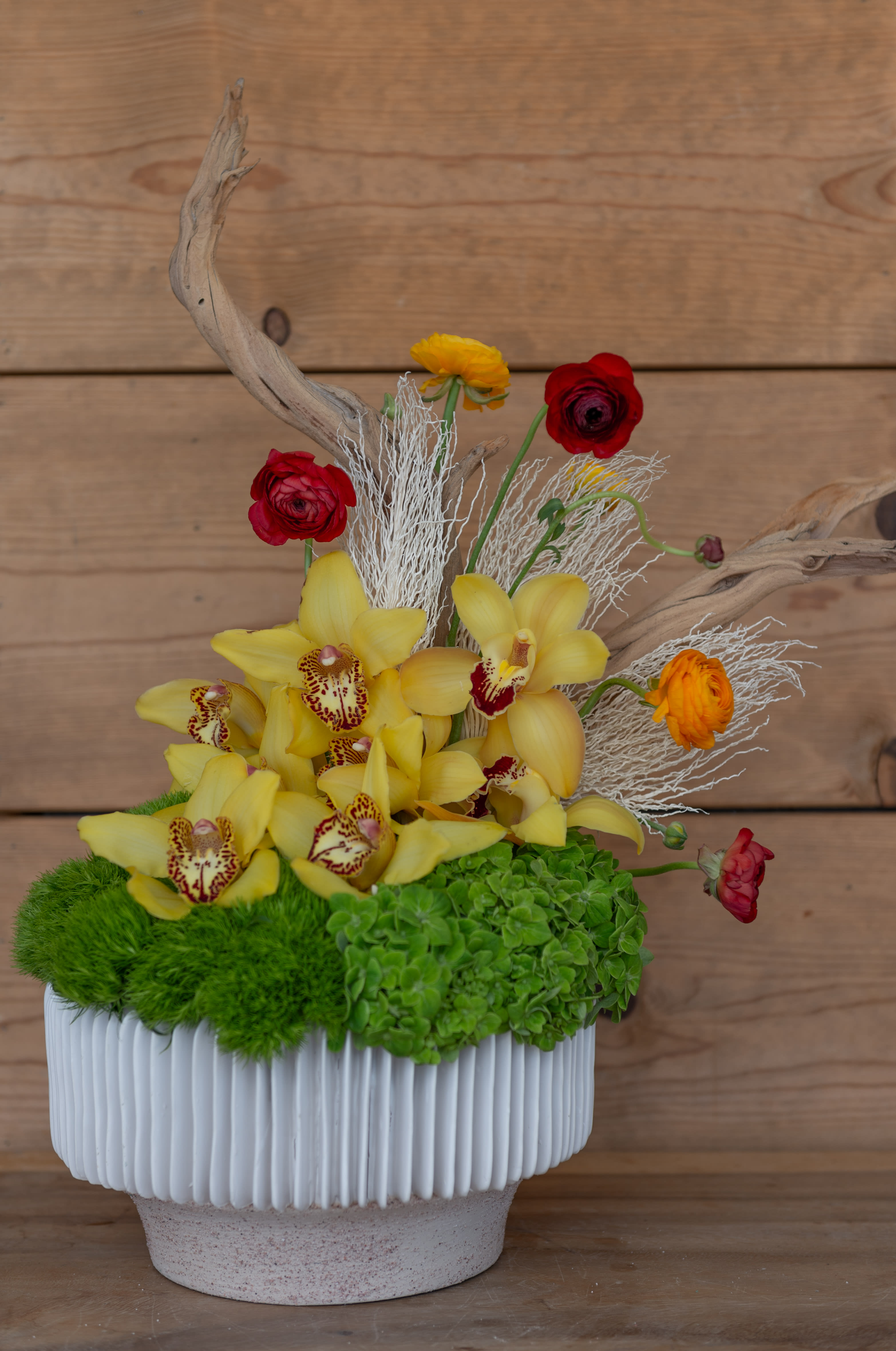 California - California is a modern arrangement delicately arranged with yellow, orange and red ranunculus a lush bed of hydrangeas sun green trick accented with drift wood. Inspired by the scenic pacific coast highway. 