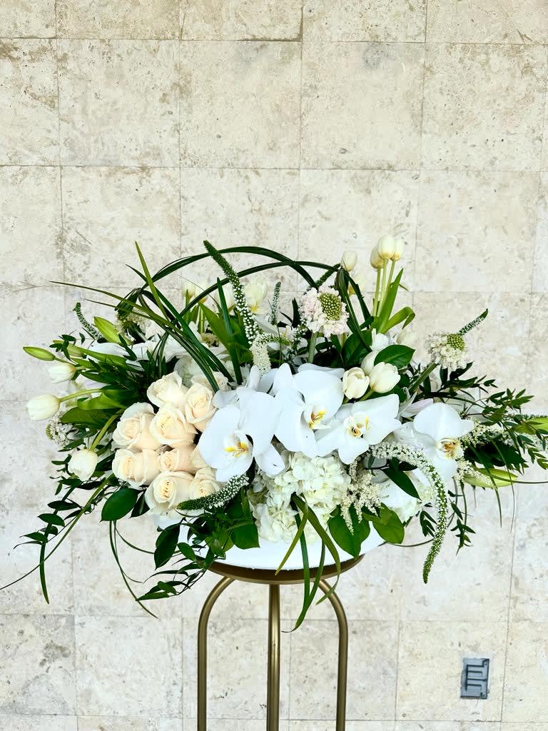 White roses and orchids arranged in a low centerpiece on a stand