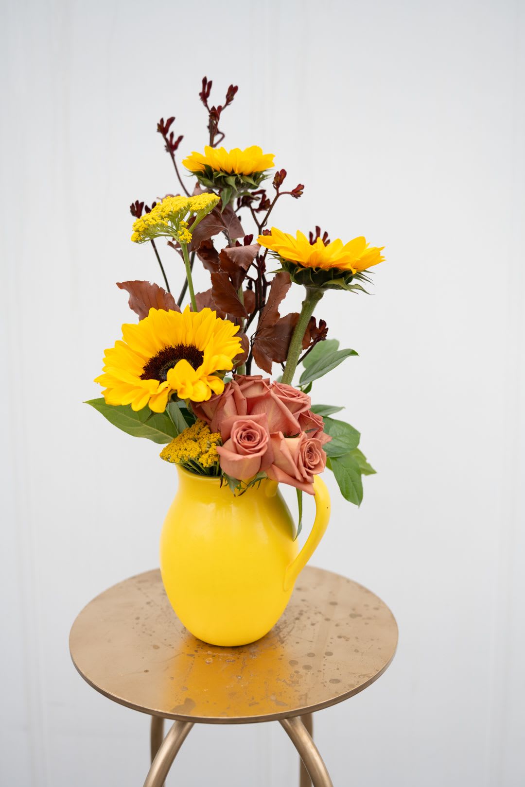 Yellow sunflowers and peach roses in a yellow pitcher vase