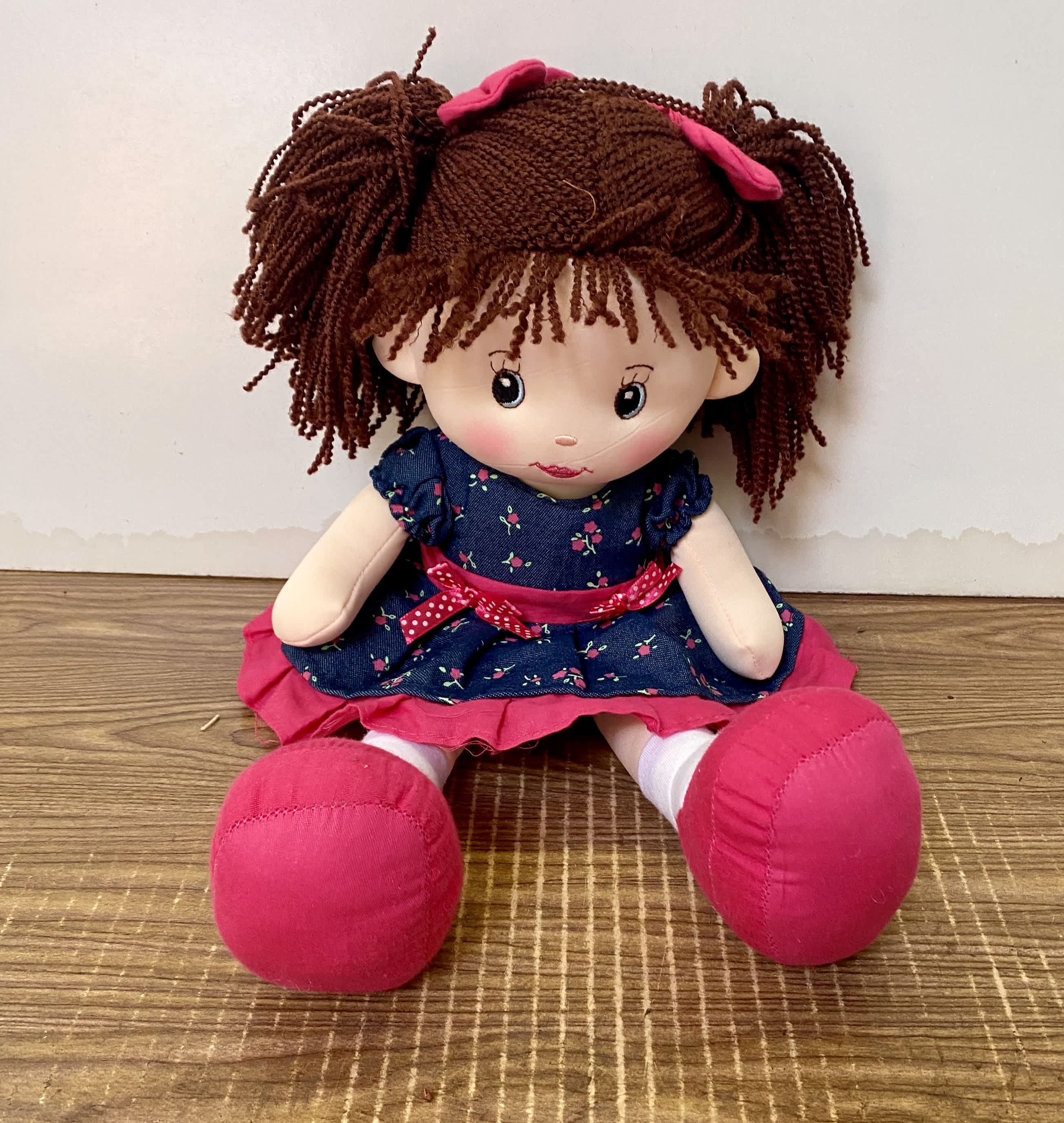 Plush doll with brown yarn hair, blue dress, and pink shoes