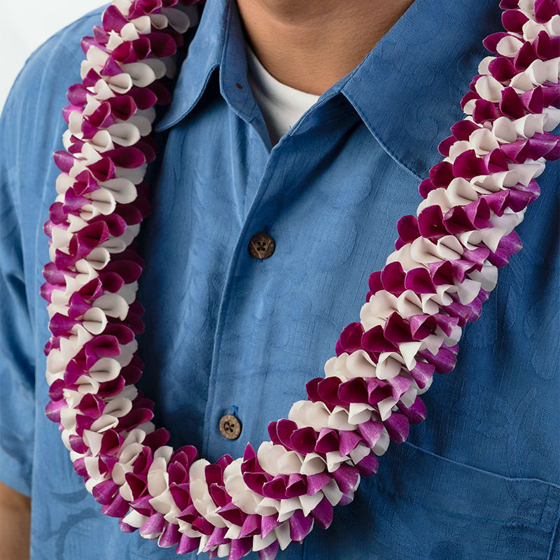 Purple and white flower lei worn around a person's neck over a blue shirt