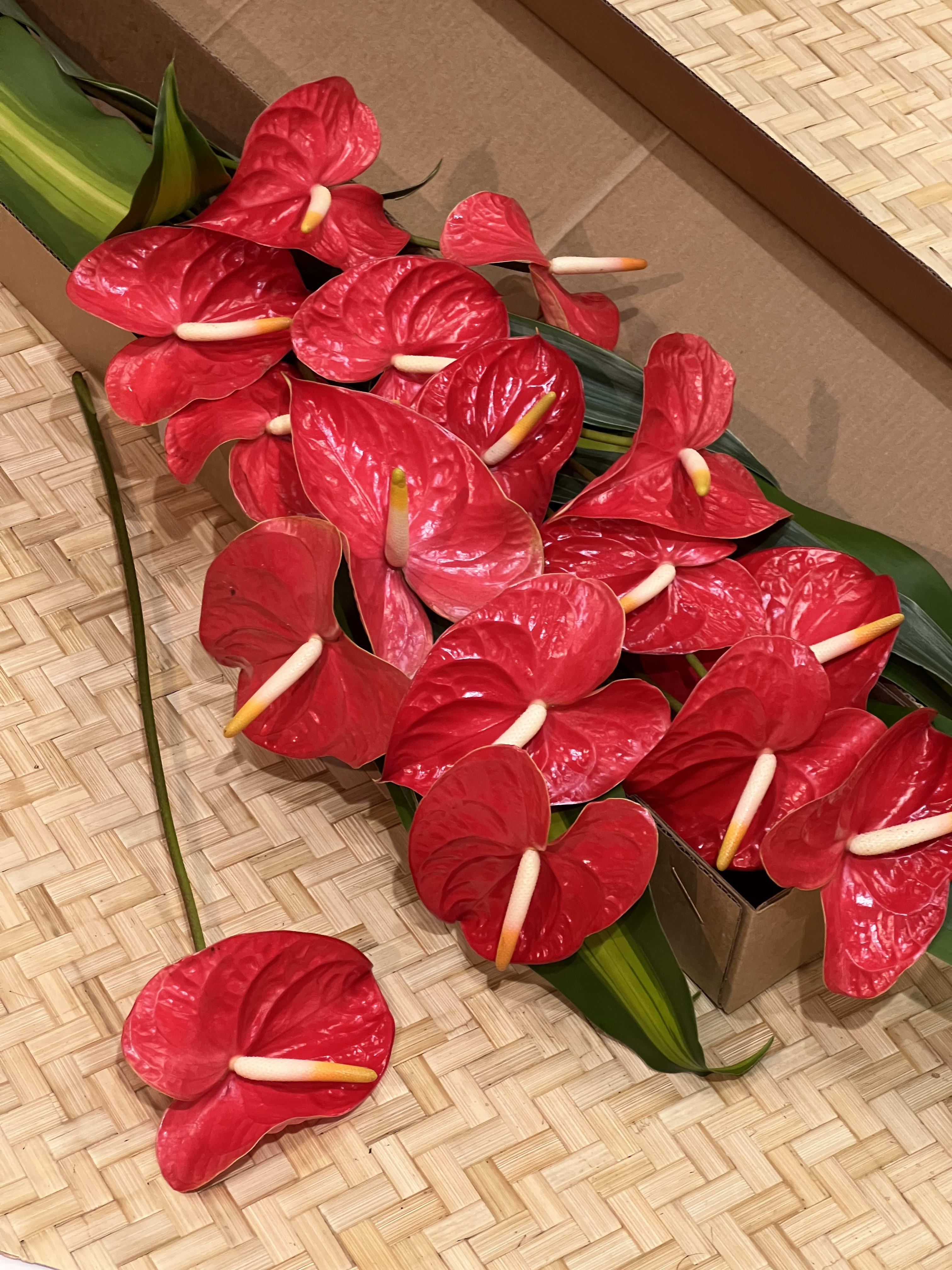 Loose red tropical flowers with pale centers packed in a shallow box on a woven mat.