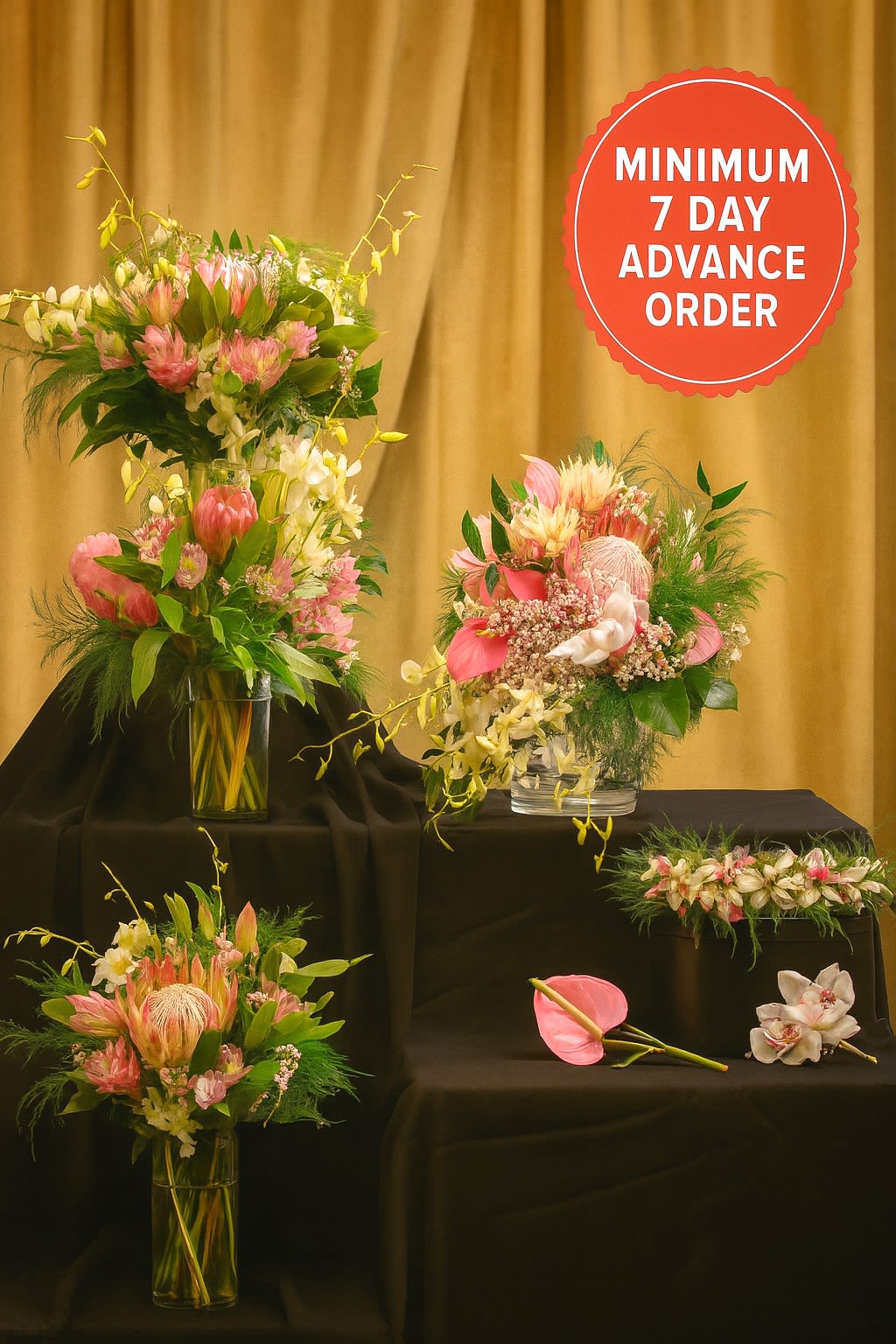 Set of pink and white tropical floral arrangements in clear glass vases on black stands.