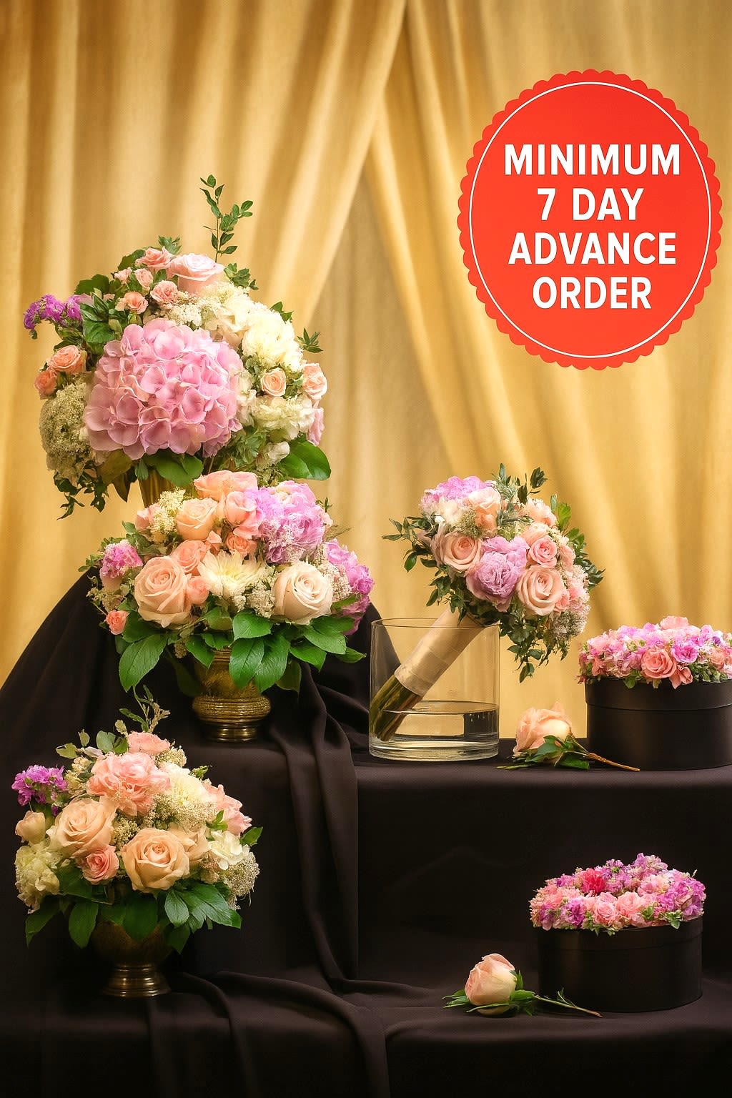 Set of blush and pink rose arrangements with hydrangeas in gold vases, boxes, and a bouquet on dark draped fabric
