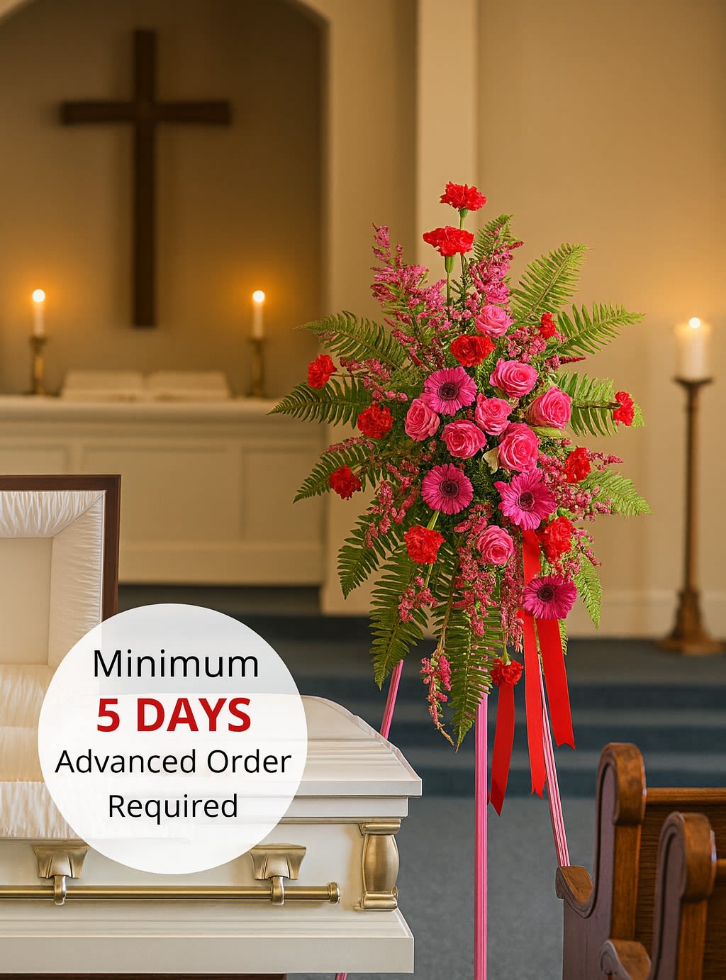 Bright pink and red standing spray on an easel beside a white casket in a chapel.