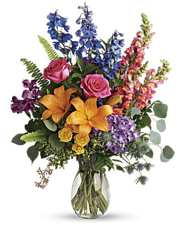 Mixed bouquet with roses, lilies, and blue and pink spikes in a glass vase