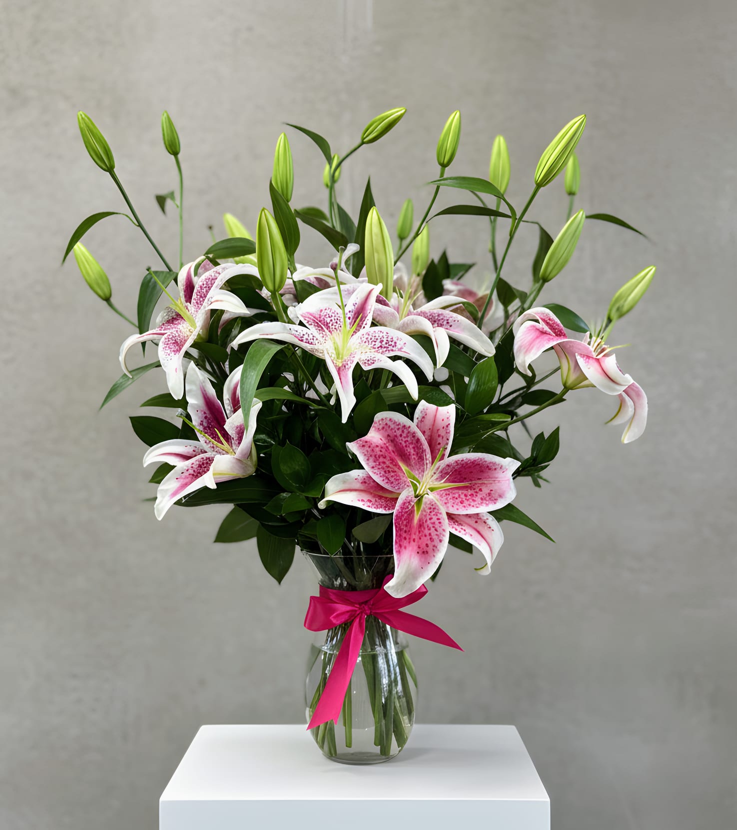 Pink and white lilies in a clear glass vase with a ribbon