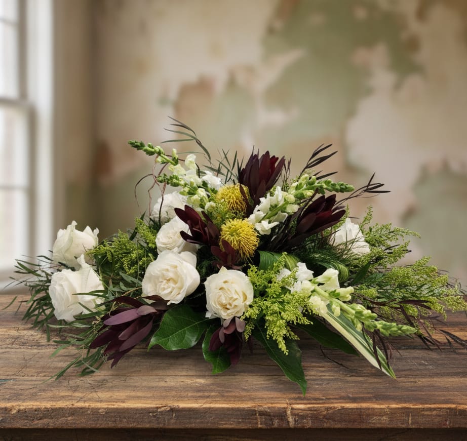 Low centerpiece of white roses, green accents, and dark burgundy blooms in an elongated design