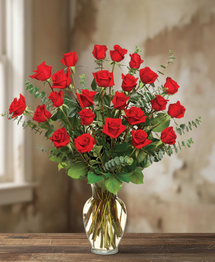 Tall arrangement of long-stem red roses in a clear glass vase on a wooden table