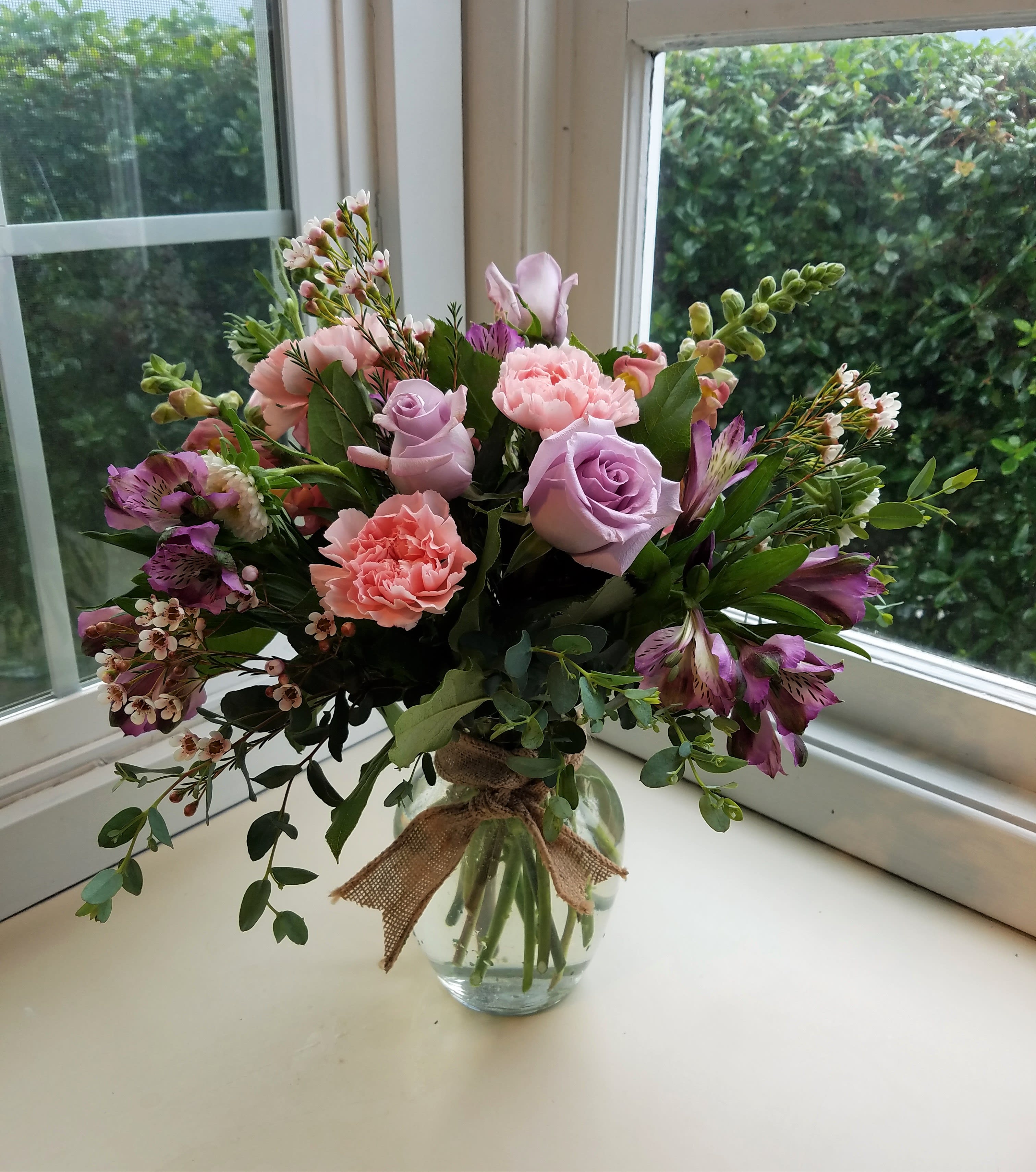 Pink and lavender bouquet in a glass vase with a burlap bow