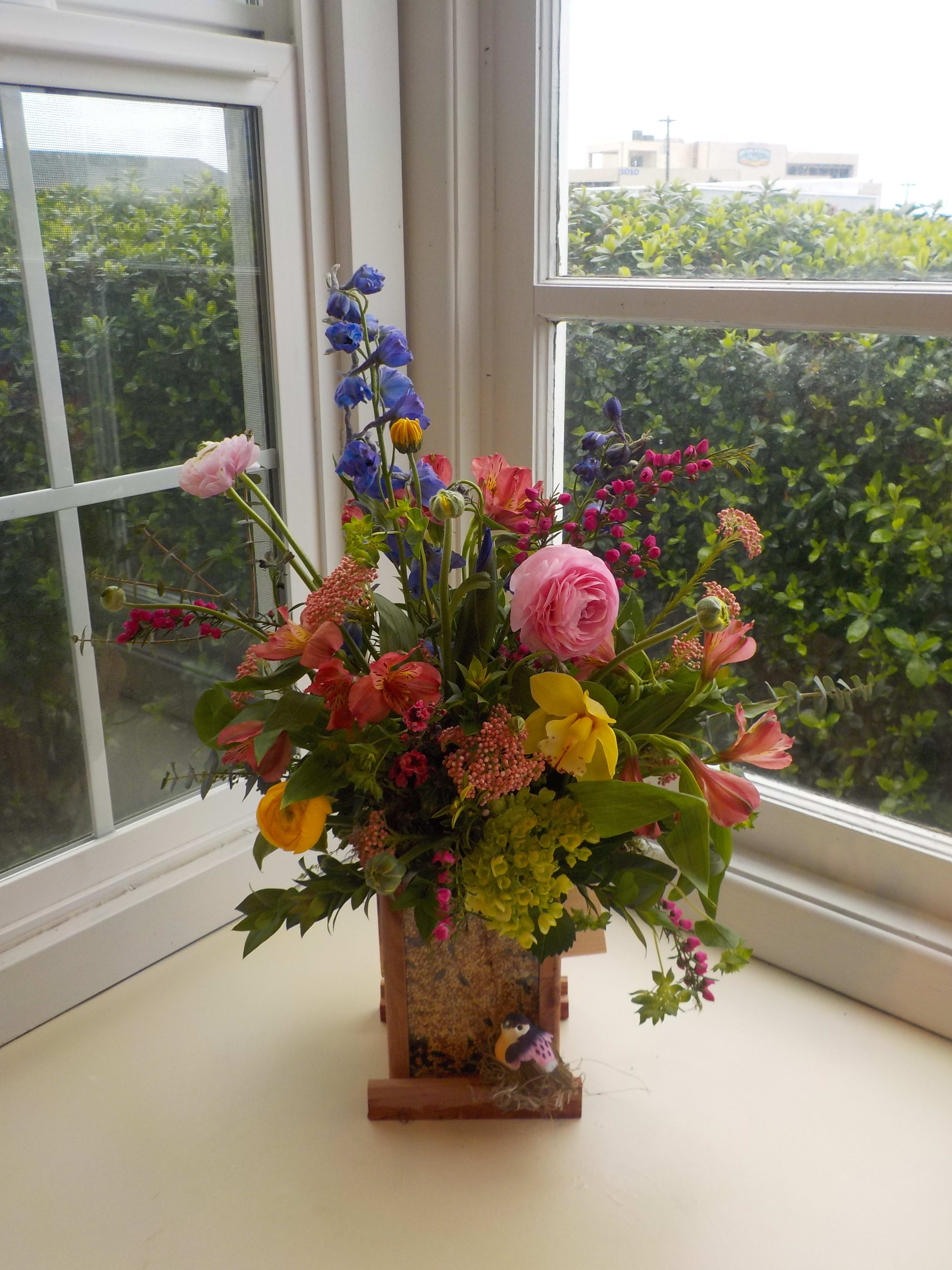 Colorful mixed flower arrangement in a wooden container on a windowsill