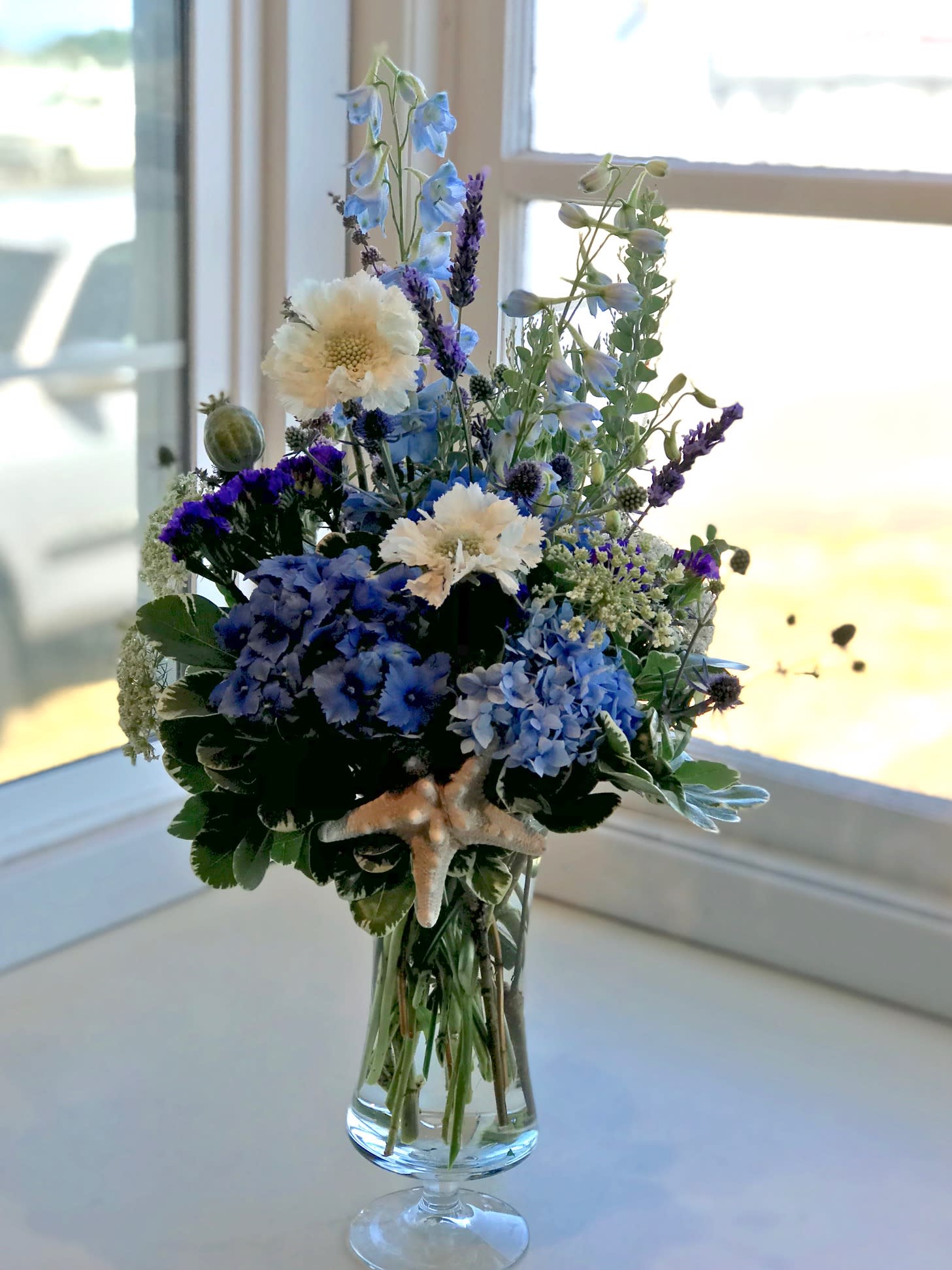 Blue and white floral arrangement in a clear glass vase with a starfish accent