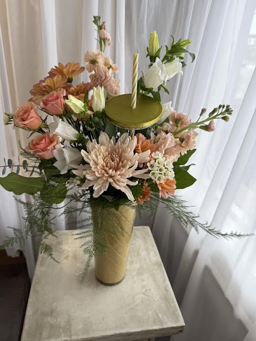 Tall floral arrangement in a gold vase with a candle on top