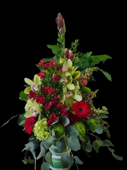 Radiant Build - Bright vertical lines of crimson gerbera daisies and red alstroemeria lift this tall flower arrangement into a bold birthday bouquet or congratulations gift that will make the person you're thinking of feel celebrated. Pale green orchids and soft green hydrangea-like blooms create a fresh, modern contrast against the reds, while trailing eucalyptus-style foliage adds a lush, garden-inspired cascade-perfect for housewarming or anyone who loves dramatic, living decor.  Arranged in a simple ceramic vase, this layered design features a dense, full base that tapers into a strong vertical silhouette. The palette of red, pink, green, and white reads vivid yet balanced: striking red focal blooms, subtle pink accents, cool green orchids, and voluminous green hydrangea-like heads surrounded by abundant greenery. The overall height and cascading texture give it a presence on mantels, entry tables, or office desks without overwhelming the space.  Choose this arrangement when you want your recipient to feel noticed and adored-ideal for birthdays, congratulations, and new-home celebrations. Vase and stem care: keep water fresh, trim stems slightly every few days, and place away from direct heat to prolong bloom life.