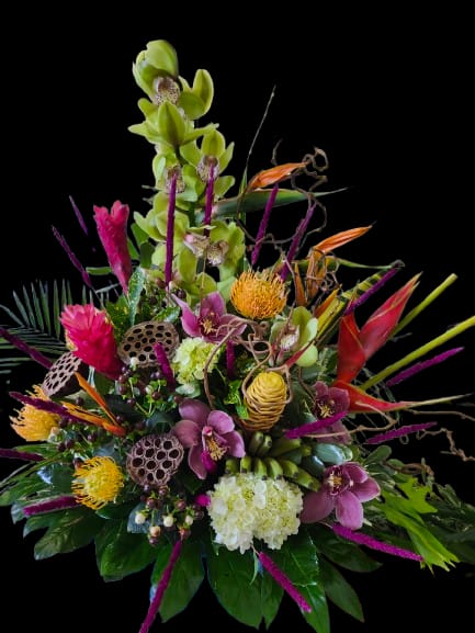 Paradise - Tall green orchid sprays crown this dramatic tropical flower arrangement, the perfect birthday bouquet or congratulations gift when you want someone to feel celebrated. Designed as an upscale everyday arrangement or a show-stopping housewarming present, the asymmetrical silhouette and vivid palette of green, purple, pink, and yellow make a confident visual statement that says "you're remarkable" to the person you're thinking of.  Dense, layered exotic blooms create a sculptural look: glossy foliage and seed-pod textures support magenta and purple hydrangea-like clusters, while orange bird-of-paradise-style forms and yellow pincushion-style blooms add punchy contrast and tactile interest. The composition reads lush and contemporary with varied heights and a mix of sleek orchid sprays and textured tropical elements, giving it presence on an entry console or dining table.  Ideal for celebrating birthdays, promotions, or a new home, this arrangement is built to impress and to last as a focal gift. Its sturdy stems and abundant foliage help support the dramatic form; refresh water daily and trim stems if needed to keep blooms vibrant. Order as a statement centerpiece for someone who delights in bold color and modern tropical style.