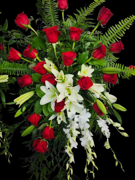 Memories - A lavish cascade of red roses, white lilies, and trailing white orchid sprays creates instant drama for a romantic bouquet or a sympathy arrangement. This large flower arrangement leans outward and downward in a graceful cascade, the vivid red and pure white palette set against abundant ferns and leafy greenery for a classic, elegant look that will make the recipient feel deeply seen and comforted.  The composition pairs dozens of red roses with open white lilies and delicate cascading orchids, layered to show off texture and movement rather than a tight, compact shape. Lush greenery and ferns fill the background and margins, giving the piece a formal, full-bodied silhouette that reads beautifully from every angle.  Perfect for anniversaries, Valentine's Day, or as a respectful sympathy tribute, this arrangement is made to convey deep emotion-passion, love, or heartfelt condolence-depending on the moment. Because of its large, cascading form, place it where the sweeping sprays can be appreciated; fresh water and a cool room will help the blooms last longer.