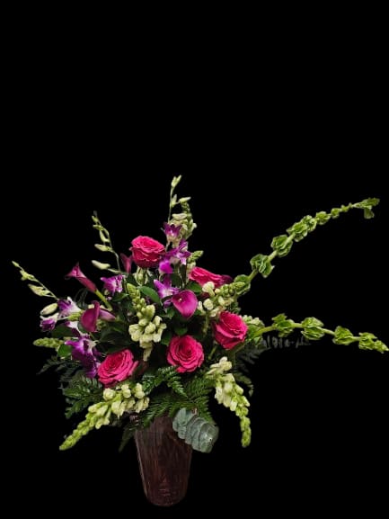 Moonlight Garden - Hot pink roses and purple orchids rise from a tall glass vase in this airy Moonlight Garden arrangement — a striking floral design perfect for birthdays, celebrations, thank-you gifts, or elegant everyday moments. Its asymmetrical silhouette and long, sculptural lines create graceful movement, giving the arrangement a modern garden-inspired feel that immediately draws the eye and makes the recipient feel truly celebrated.  The design combines vibrant roses, delicate orchid blooms, white snapdragons, and sculptural green Bells of Ireland with soft white accents and fresh foliage for texture and contrast. Arranged in a clear glass vase, the composition feels dramatic yet refined, with airy spacing and vertical movement that give it presence without feeling heavy. The layered textures of orchids, snapdragons, and lush greenery create a fresh, artistic look suited for dining tables, entryways, or statement gifting.  Elegant, expressive, and full of movement, Moonlight Garden is designed for anyone who appreciates contemporary floral styling with a romantic edge. To prolong bloom life, refresh water regularly, trim stems slightly every few days, and keep away from direct heat and sunlight.