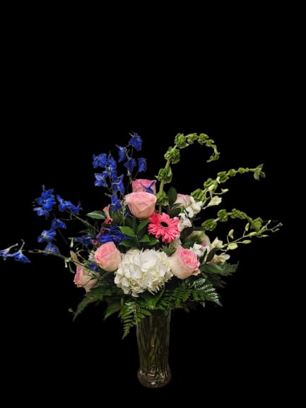 Blue Rhapsody - Soft pink garden roses and lush white hydrangeas are paired with airy blue delphinium and delicate white orchids in this elegant garden-style arrangement — perfect for birthdays, thank-you gifts, spring celebrations, or refined everyday moments. The asymmetrical silhouette and naturally arching stems create graceful movement and a light, romantic presence that makes the recipient feel truly noticed and celebrated.  Arranged in a clear glass vase, the palette of blush pink, crisp white, vivid blue, and fresh greenery feels fresh, uplifting, and effortlessly elegant. Layered textures from velvety garden roses, cloud-like hydrangea blooms, airy delphinium spires, and delicate orchid petals create depth and softness while maintaining an organic, airy composition. Designed for dining tables, mantels, or entryways, the arrangement brings a sophisticated garden-inspired feel to any space.  Fresh, expressive, and full of natural movement, this arrangement arrives ready to display. To prolong bloom life, refresh water regularly, trim stems slightly every few days, and keep away from direct heat and sunlight.