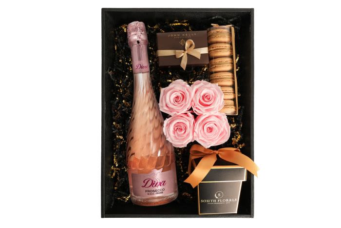 Gift box with pink sparkling wine, pink roses, macarons, and chocolates
