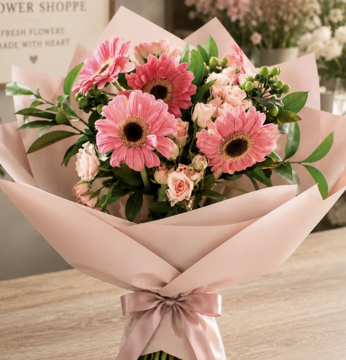 Pink gerbera daisy and rose bouquet wrapped in blush paper with a ribbon