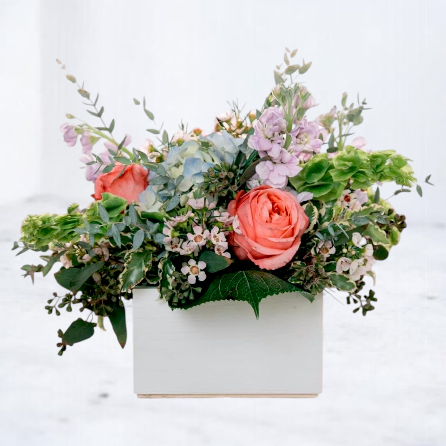 Field Notes - Field Notes captures the beauty of flowers discovered along the way. Designed with an airy mix of premium seasonal blooms, delicate textures, and fresh greenery, this arrangement feels naturally gathered and thoughtfully composed.  Soft coral roses mingle with pastel blooms, botanical accents, and lush foliage to create a design full of movement and character. Arranged in a modern wooden box, Field Notes brings a fresh, organic aesthetic that feels equally at home on a dining table, desk, or entryway.  Its relaxed garden-inspired style makes it a versatile choice for birthdays, thank-you gifts, housewarmings, celebrations, or simply letting someone know they're on your mind. Every arrangement is handcrafted by the designers at Whiskey Wallflower using the freshest flowers available.  While flower varieties may vary seasonally, the overall color palette, style, and value will remain true to the design shown.
