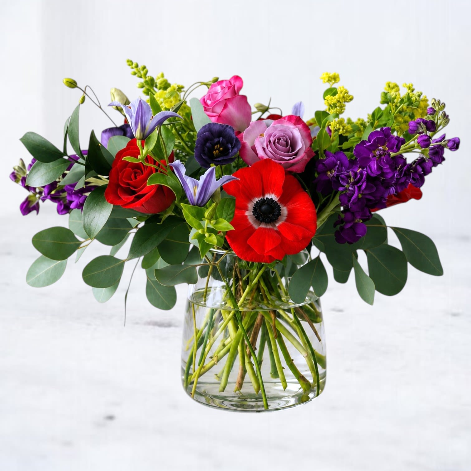 Mixed bouquet of red, pink, purple, and yellow flowers in a clear glass vase