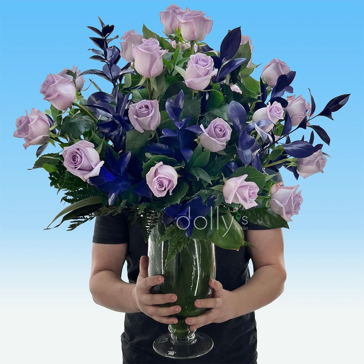 Classic 3 Dozen Lavender Long-Stem Roses - Pale lavender long-stem roses take center stage in this classic 36-stem arrangement, a graceful choice for an anniversary bouquet, romantic gift, or a refined sympathy or celebration arrangement. The soft purple blooms read as romantic and serene, while deep purple foliage and rich green leaves add dramatic contrast so the person you're thinking of will feel truly seen and cherished.  Arranged upright in a tall clear glass vase, the design presents a full, rounded silhouette with roses spreading broadly above the rim for a formal, elegant look. The palette mixes lavender roses with dark purple accent foliage, fresh greenery and touches of white and pink tones for subtle dimensional color - all gathered to showcase the long stems and open blooms. The glass vase keeps the focus on the flowers and suits a bedside table, dining centerpiece, or mantel.  Perfect for anniversaries, birthdays, or a thoughtful just-because surprise, this bouquet reads as both romantic and sophisticated; it also works as a tasteful sympathy piece when you want to convey comfort. Vase included; trim stems and refresh water every 2-3 days to keep the roses looking their best.
