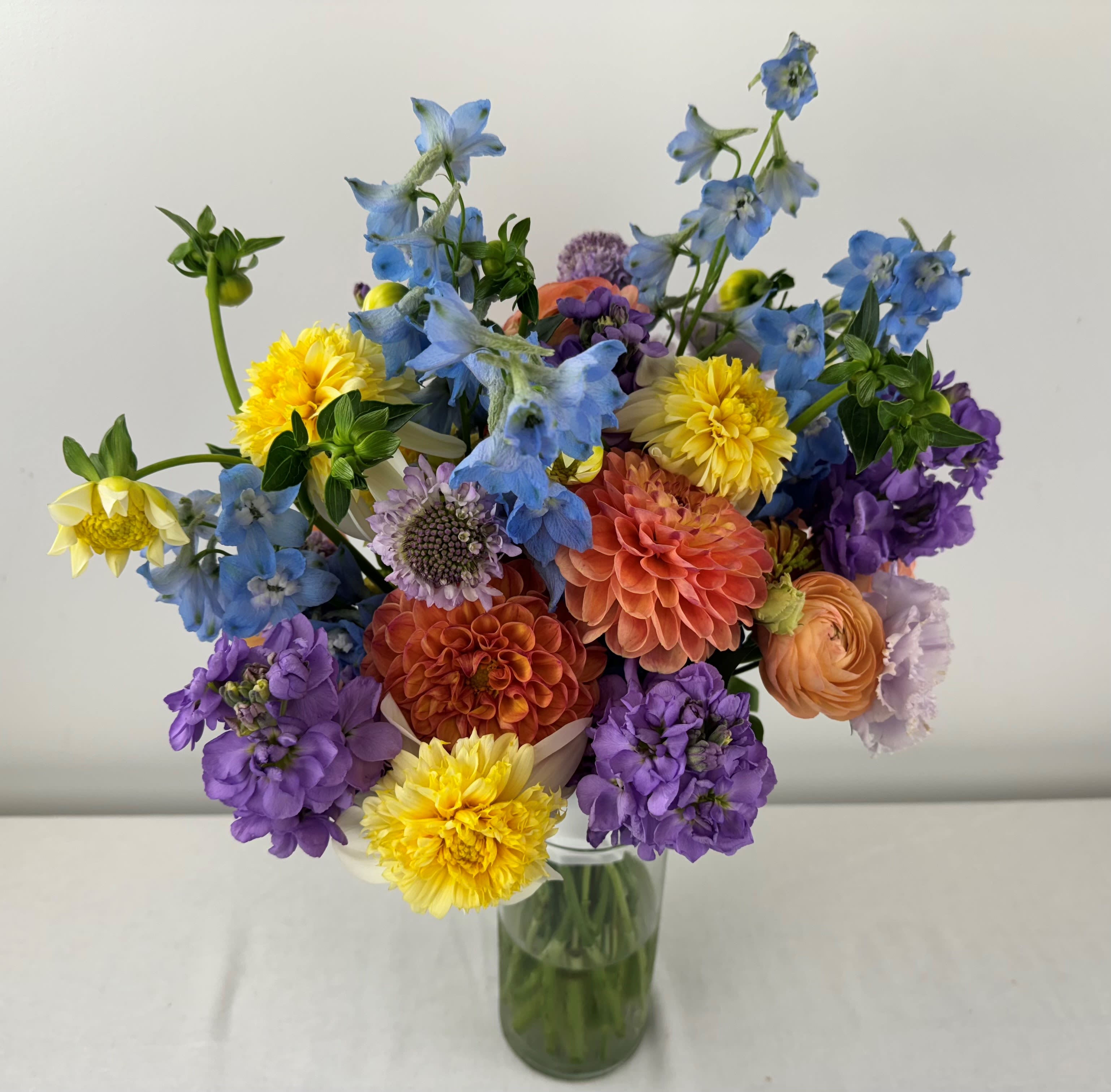 Mixed bouquet of blue, purple, yellow, and peach flowers in a glass vase