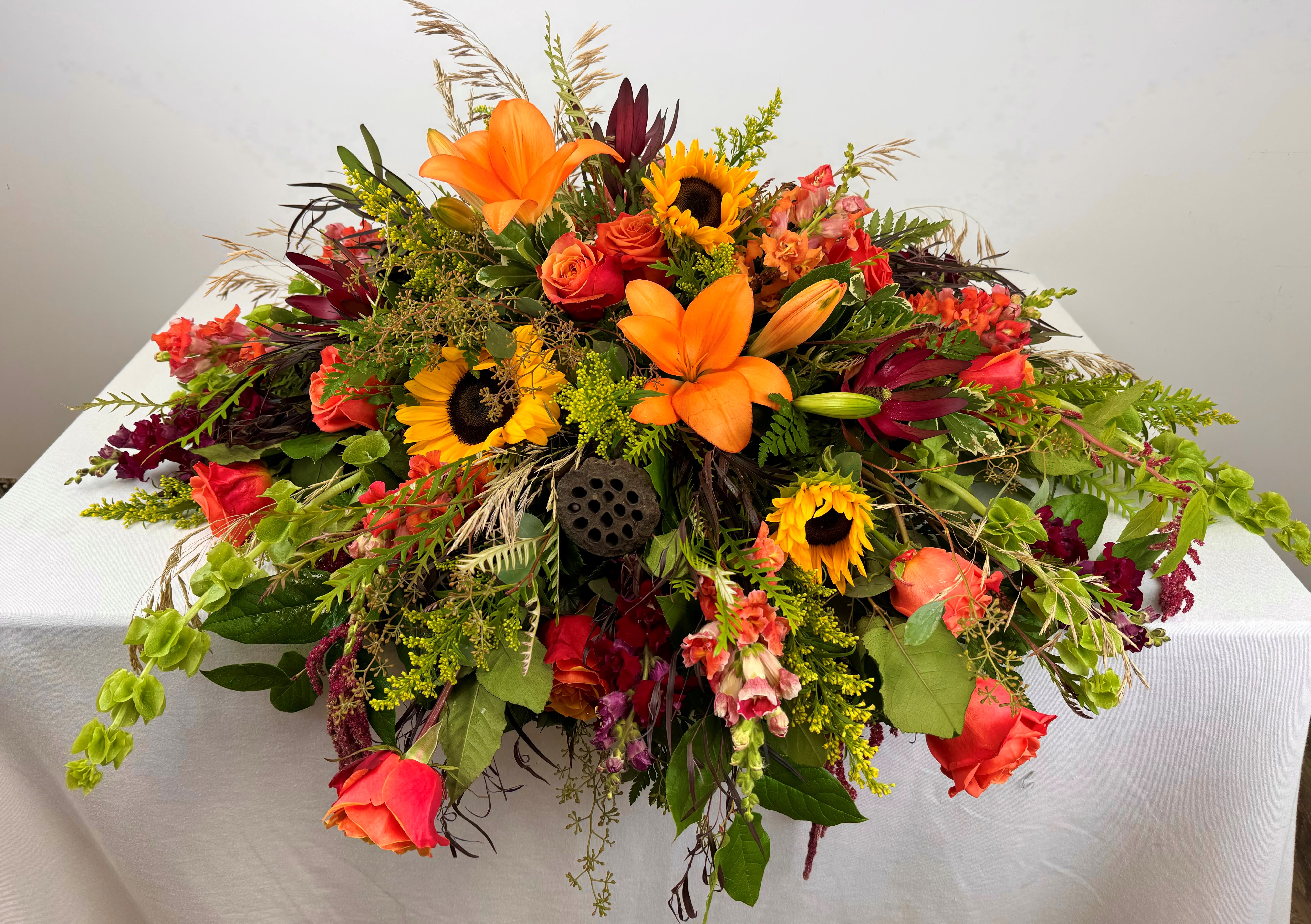 Large arrangement of orange lilies, sunflowers, and roses on a table