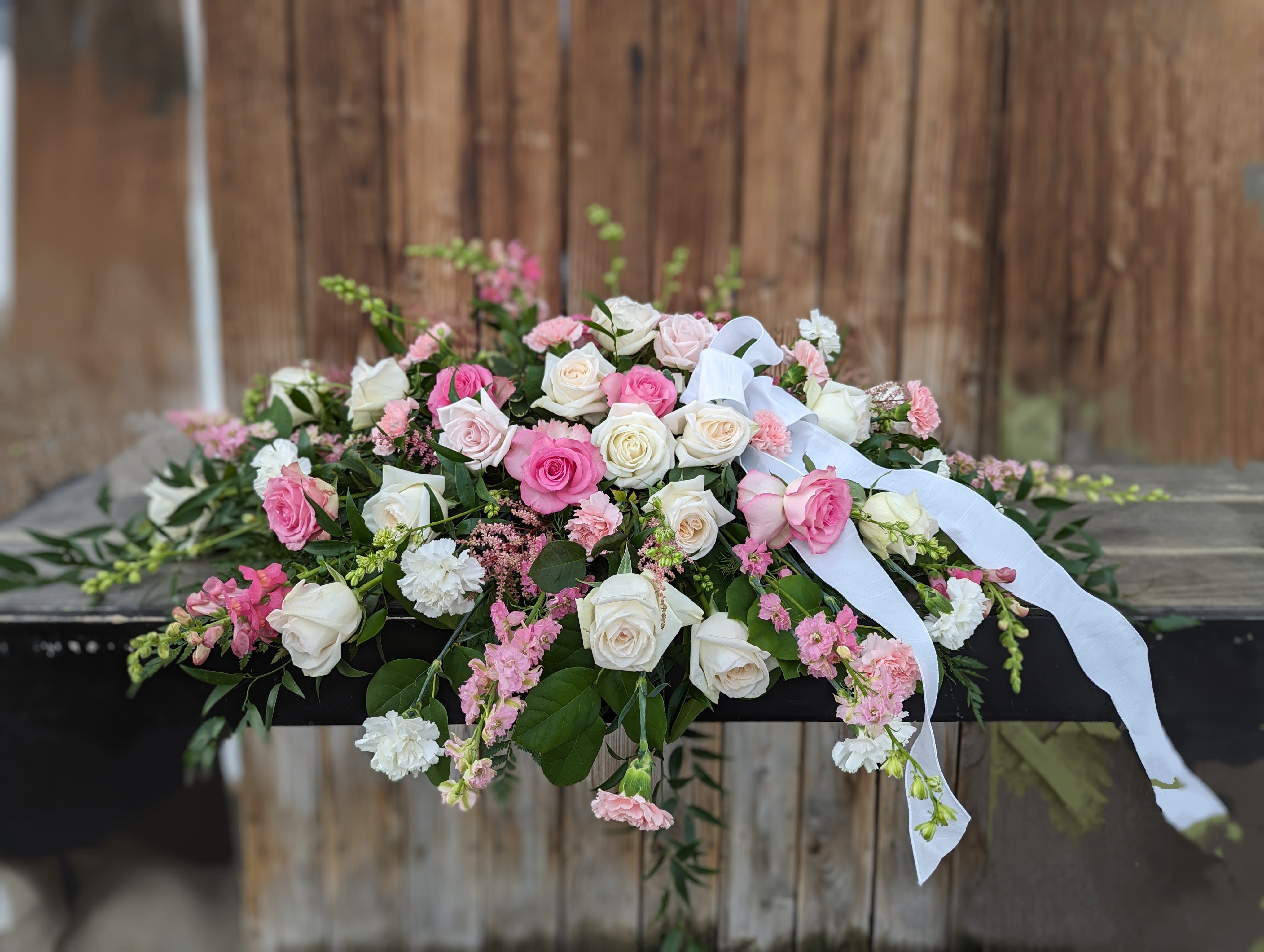 Pink and white rose arrangement with ribbon draped over a dark casket
