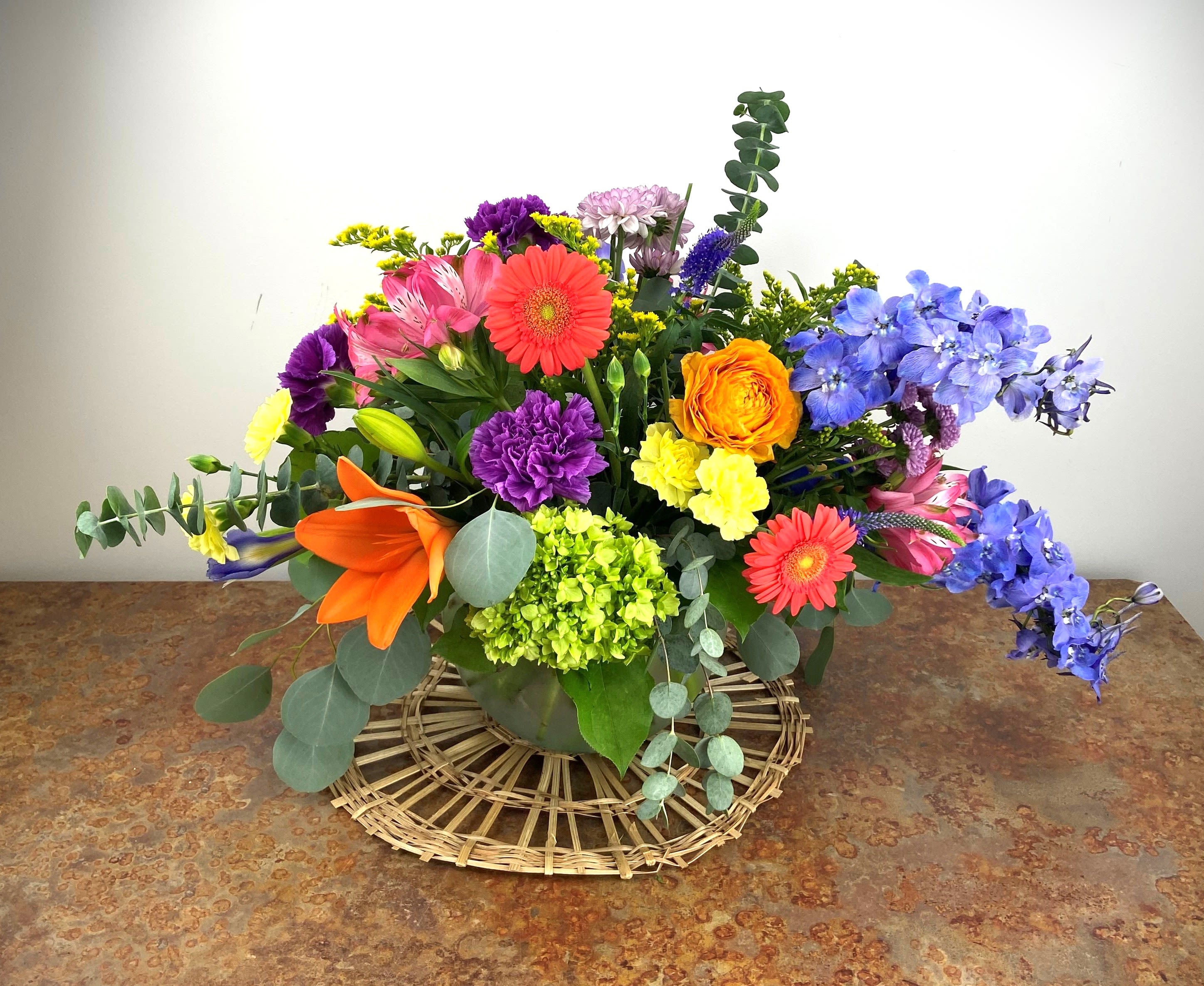Colorful mixed bouquet in a low vase with orange, blue, pink, and purple blooms