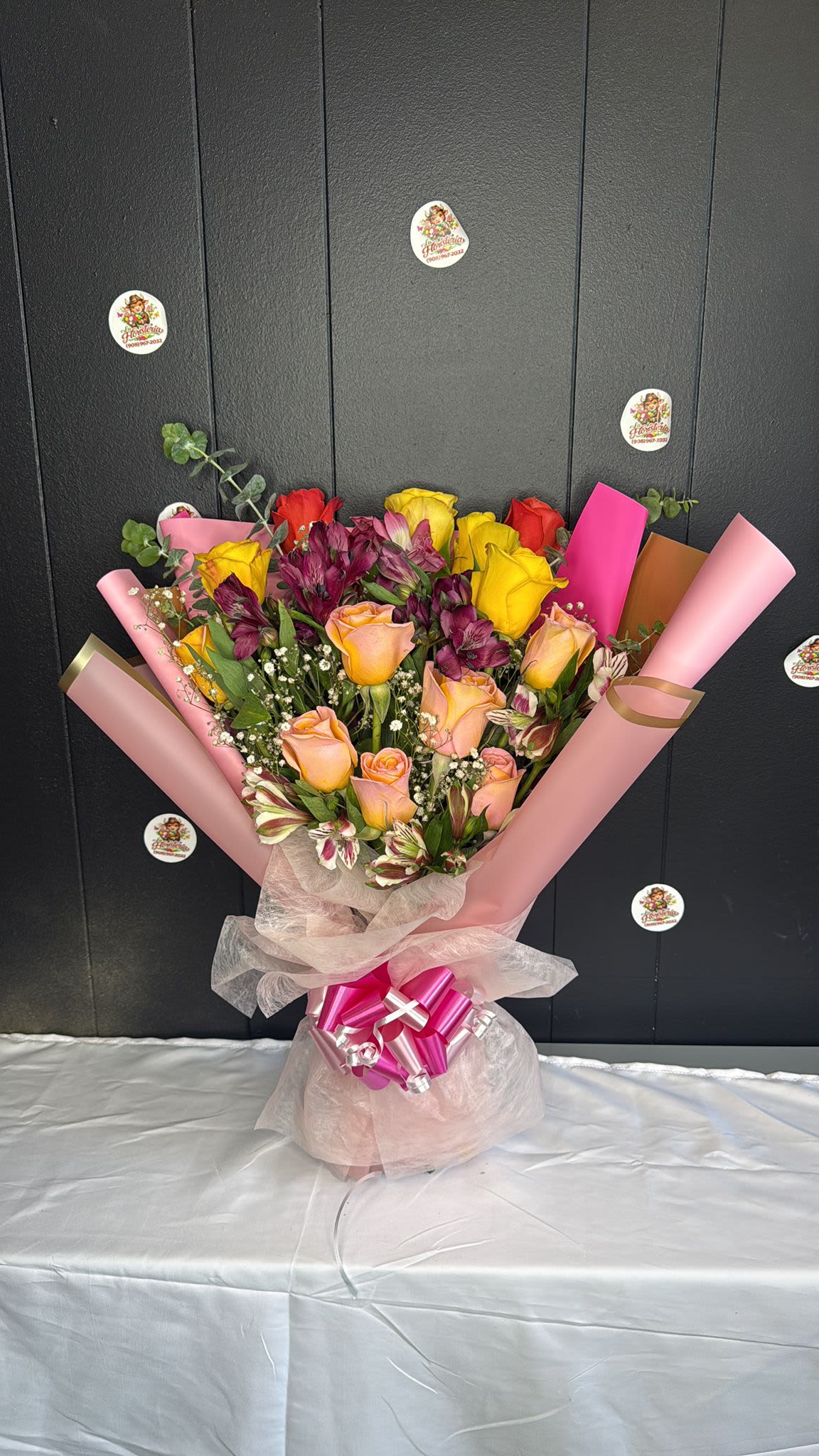 rosas coloridas  - A bright, celebratory mix of colorful roses makes this flower arrangement the perfect birthday bouquet or anniversary gift that will make the person you're thinking of feel genuinely celebrated. Rosas coloridas pairs peach, yellow, red and pink roses with deep purple alstroemeria and delicate white filler blooms for a cheerful yet polished look-ideal for congratulations, romantic notes, or simply to brighten someone's day.  The arrangement is gathered into a full, upright composition and wrapped in layered pink paper with a soft translucent mesh overlay, finished with a large shiny pink ribbon bow at the base for a gift-ready presentation. Textures play nicely together-the velvety roses, the starry alstroemeria petals, and the airy filler-creating a lush, hand-tied feel that reads beautifully from every angle.  Designed to deliver an immediate smile, this bouquet suits recipients who appreciate bold color and romantic touches-partners, friends celebrating milestones, or anyone needing a joyful pick-me-up. Order with standard care: keep blooms in fresh water, out of direct sun and drafts, and trim stems slightly if arranged in a vase to extend enjoyment.