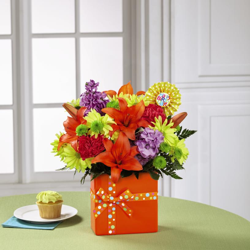 The FTD Set to Celebrate Birthday Bouquet - The FTDÂ¨ Set to CelebrateÂª Birthday Bouquet is ready to take their birthday celebration to the next level with a bright burst of color and perfectly arranged fresh blooms! Popping with personality and style, this flower bouquet brings together orange Asiatic Lilies, hot pink roses, lavender gilly flower, hot pink carnations, yellow traditional daisies, green button poms, and lush greens. Presented in a modern rectangular orange ceramic vase tied with a polka dotted orange ribbon to give it the look of a birthday present, this flower arrangement is then accented with a "Happy Birthday" pick to give it that ultimate party style. GOOD bouquet includes 10 stems. Approx. 15"H x 12"W. BETTER bouquet includes 14 stems. Approx. 16"H x 13"W. BEST bouquet includes 18 stems. Approx. 17"H x 14"W. EXQUISITE bouquet includes 18 stems. Approx. 17"H x 15"W.