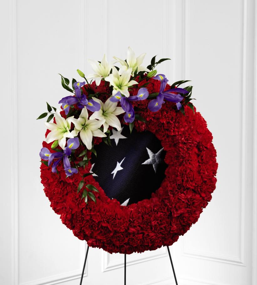 FTD To Honor One's Country Wreath - The FTD To Honor One's Country Wreath is a vibrant patriotic   tribute to a fallen soldier. Red carnations form a gorgeous wreath,   accented with blue iris and white Asiatic lilies, which encircles a blue   fabric with white stars on it, in character with the American flag, to   create a stunning display for their final farewell service. Displayed on   a wire easel.      26""h x 22""w