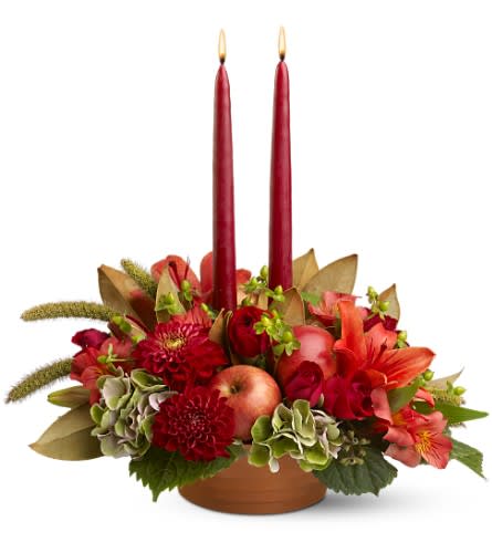 Autumn Twilight - At twilight, a soft evening light settles over the fields, and there's a hush in the garden. The subtle mix of this lovely harvest centerpiece includes red roses, lilies and dahlias, plus unique trimmings like real apples, dried millet and magnolia leaves. Two tall red tapers will cast a pretty light over the Thanksgiving feast or any festive occasion.    Red dahlias, spray roses, Asiatic lilies and alstroemeria, plus green hydrangea and hypericum â accented with magnolia and galax leaves, seeded eucalyptus, real apples and dried millet â are arranged in a clay pot with two 12â red tapers.    Approximately 16" (W) x 15" (H)    Orientation: All-Around    As Shown : TFWEB226