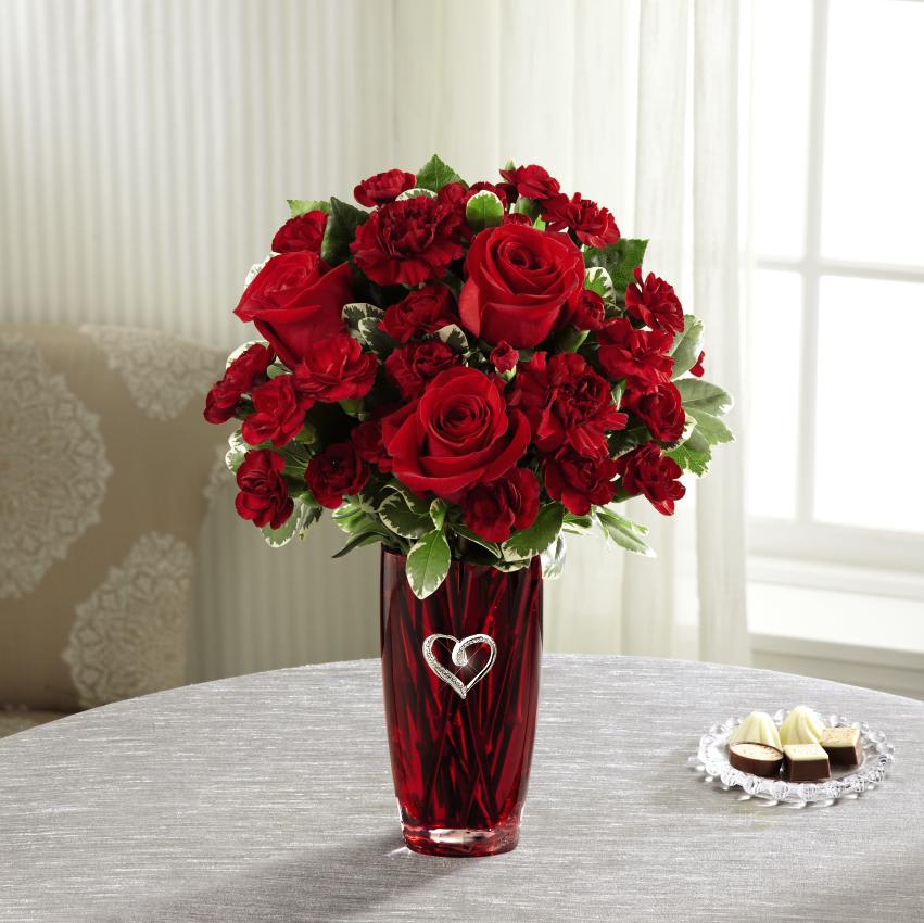 Sweethearts Bouquet - When you're "red-dy" for romance, this rich, lush bouquet of vibrant red makes a sure-fire way to let that special someone know. This brilliant burst of red and burgundy carnations and red roses (in Deluxe, Premium, and Exquisite versions) are individually hand-selected and hand-arranged by an FTD artisan florist in a heavy, red glass vase embellished with a modern, silvery metal heart clip that can be removed and cherished as a loving keepsake of this magnificent bouquet.
