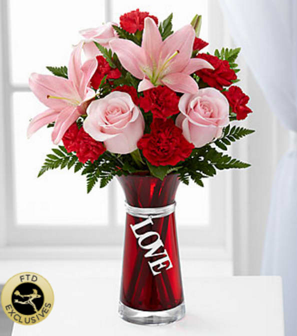 The FTD® Hold My Heart™ Bouquet - The FTD® Hold My Heart™ Bouquet is a bold statement of love's connection to delight your sweetheart this coming Valentine's Day. Unforgettable pink roses and pink Asiatic Lilies are offset by the rich reds of carnations and mini carnations perfectly accented with lush greens to create an exceptional fresh flower arrangement. Presented in a designer red glass vase with a large silver toned charm dangling from the neck, declaring, "Love," this mixed flower bouquet will be a wonderful way to express your undying love and affection and add a touch of romance to their February 14th. Your purchase includes a complimentary personalized gift message.
