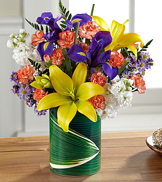 The FTD® Sunlit Wishes™ Bouquet - LF4S  Bright, crisp and high contrast flowers are combined in a lively, happy-making bouquet that's a treat to give or get for any reason at all. Yellow Asiatic lilies, purple iris, white stock, lavender Monte Casino and orange mini carnations are arranged in a ceramic "illusion" vase that convincingly replicates the look of a leaf-lined glass pillar. It's an arrangement sure to cast a golden glow to make any day one that's special and memorable. 