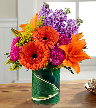 The FTD® Sunset Sweetness™ Bouquet - LF1S  Take a quick and fun spin around the color wheel with a bouquet of bright, vibrant shades spanning a sunset spectrum from orange through purple. Asiatic lilies, Gerbera daisies, magenta carnations, purple stock and more are arranged in a ceramic "illusion" vase that convincingly replicates the look of a leaf-lined glass pillar. It's an arrangement sure to make some lucky someone's day while burnishing your credentials as a most creative gift giver.