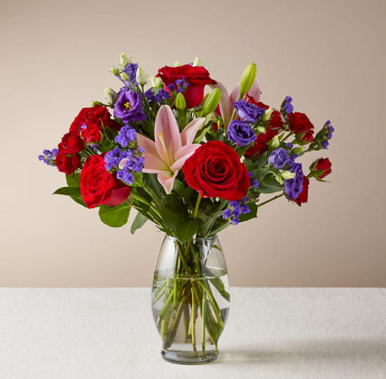 Truly Stunning Bouquet - This dreamy jewel toned bouquet combines bold color and eye catching texture to make a statement. Featuring a thoughtful array of both roses and lilies, this dazzling assortment is bound to impress your recipient.  The Deluxe Bouquet is approximately 14"H x 16"W.