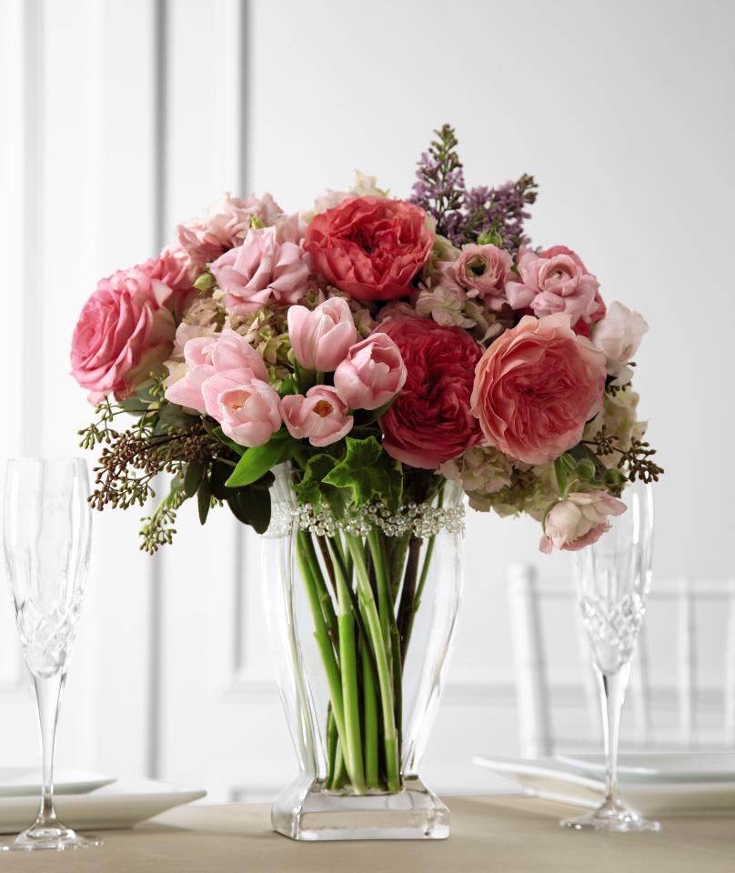 FTD Abundant Array Arrangement - The FTD Abundant Array Arrangement is full of romantic intrigue and   sweet beauty to offer its exquisite color and texture to your wedding   celebration. Pink garden roses, ranunculus, tulips, and double   lisianthus are accented with blush hydrangea, purple lilac, seeded   eucalyptus, and variegated ivy, all gorgeously arranged in a tall clear   glass vase to bring a special ambiance to your big day. Approx. 18âH x   12W.   